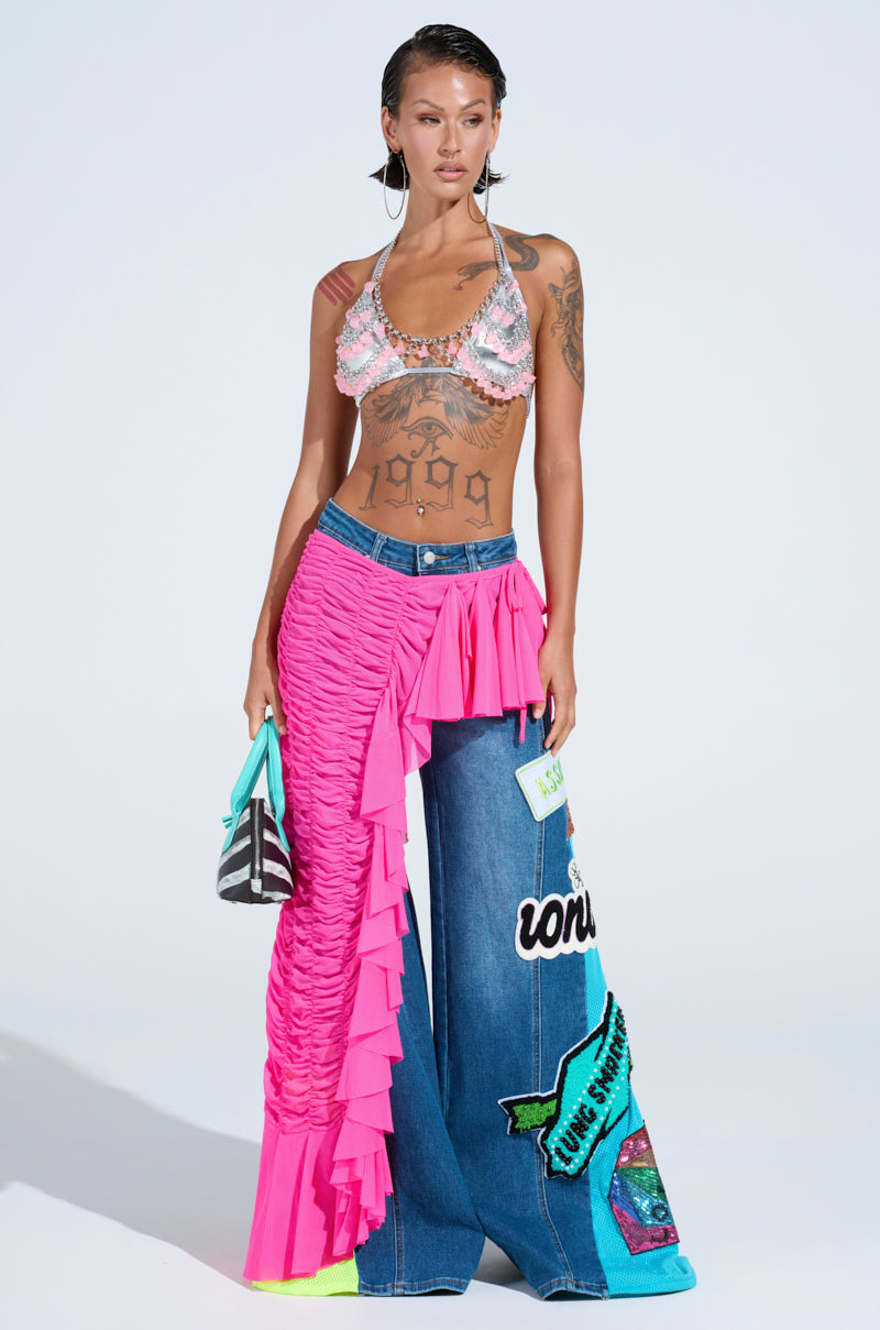 A woman poses in the LAYERED UP MESH RUFFLE BELT SKIRT, styled with a crochet bikini top, wide-leg patchwork denim pants, striped mini bag, and large hoop earrings—her festival-ready look is bold and eye-catching.
