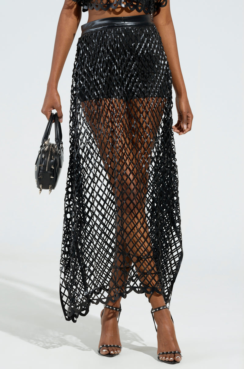 A person wearing the elegant BREAKING THROUGH MAXI SKIRT in black, layered over black shorts, holds a handbag. They also sport chic strappy black high heels against a plain, light-colored background.