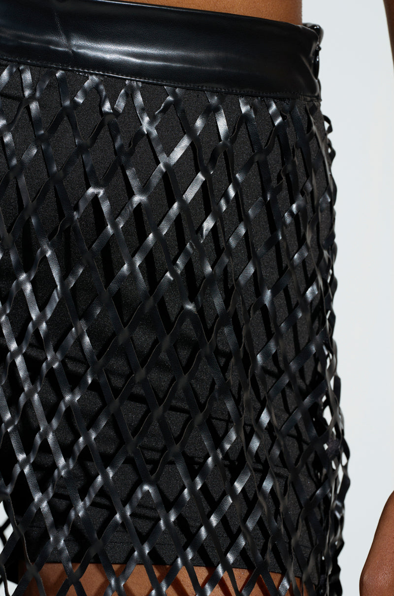 Close-up of a fashion design featuring the BREAKING THROUGH MAXI SKIRT, prominent with its cage-inspired design. The underlying fabric appears smooth, while the glossy, crisscrossed strips create a textured, geometric look reminiscent of an elegant faux leather finish.