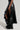 Against a light gray background, an individual models the KEEP WALKING MIDI SKIRT, a high-rise black leather piece featuring a side slit, paired with black knee-high studded boots.