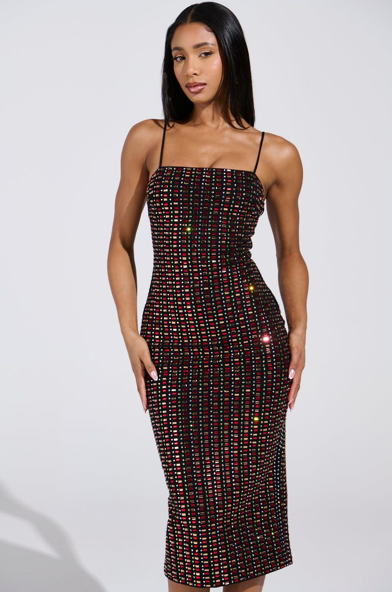 A woman poses confidently in the sleek RENEE RHINESTONE MIDI DRESS, against a plain backdrop. The black bodycon dress boasts colorful, sparkling vertical lines and thin straps. She has straight, shoulder-length hair and gazes directly at the camera.