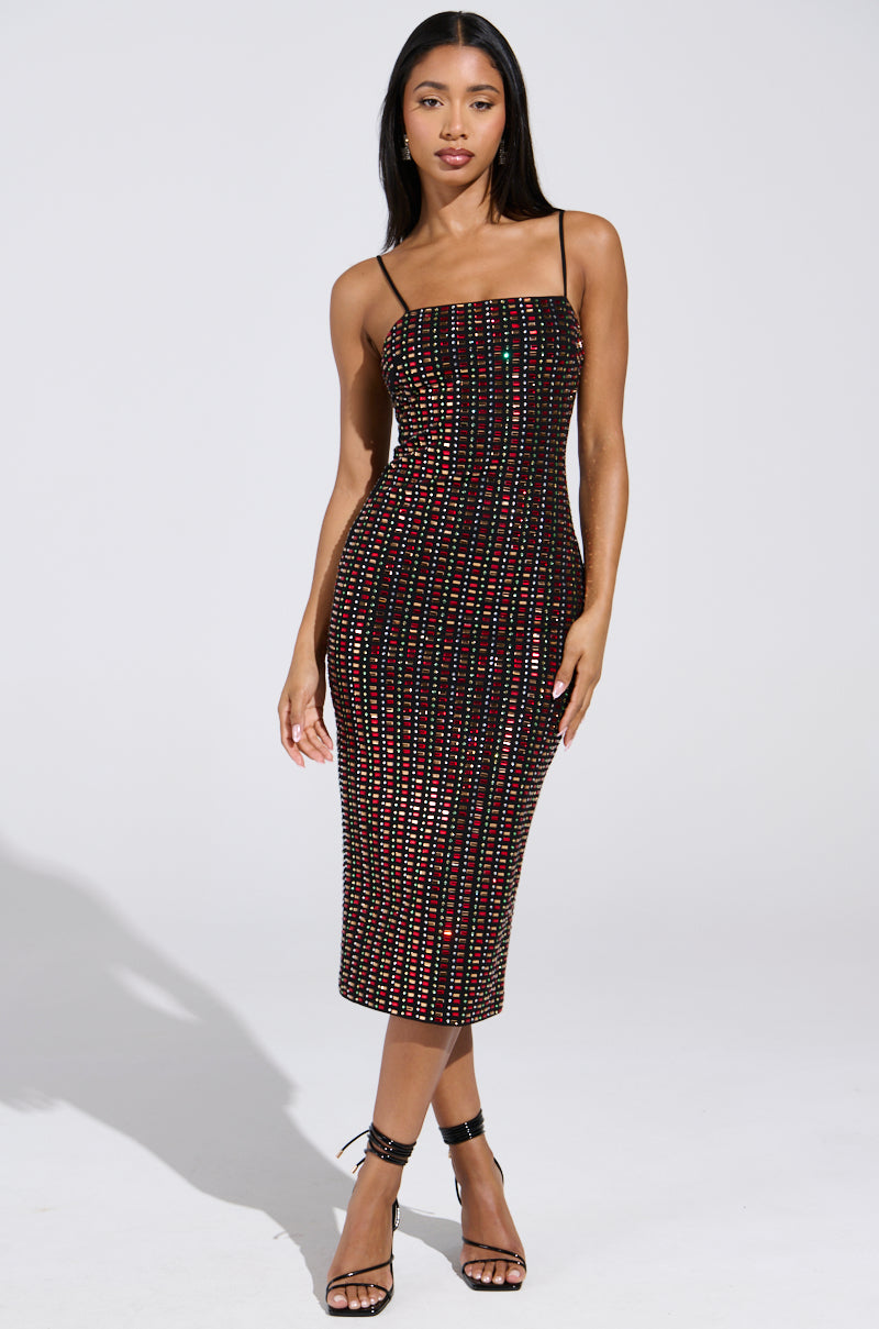 A woman models the RENEE RHINESTONE MIDI DRESS, featuring a vibrant, multicolored design with thin straps, on a plain background. Her long, straight hair enhances the bodycon fit, and she completes her ensemble with elegant black strappy heels.