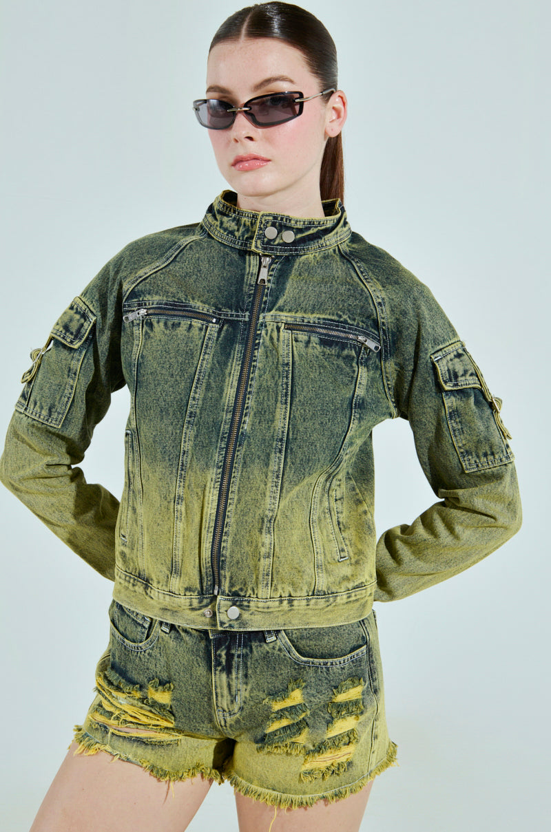 A person exudes confidence in the CALL ME CRAZY DENIM MOTO jacket and matching distressed shorts. Their long hair is tied back, and they wear sunglasses against a plain background.