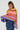 A person with long braided hair poses in the LOOK AT ME CHUNKY MULTI COLOR KNIT SWEATER, highlighting its oversized silhouette and vibrant rainbow striped pattern. This eye-catching piece pairs seamlessly with a high-waisted denim skirt, set against a simple white background.