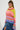 With long braided hair, a person flaunts an oversized silhouette in the LOOK AT ME CHUNKY MULTI COLOR KNIT SWEATER, showcasing a vibrant blend of rainbow stripes in yellow, orange, pink, and purple. Paired with a blue denim skirt, they pose confidently against a plain background.