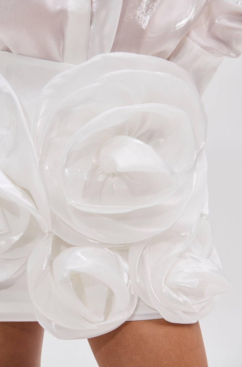 Close-up of the PRETTY HOT MINI SKIRT in shiny white, featuring large sculpted rose appliques. The glossy fabric gives it a delicate, floral look, shown worn with bare legs. 8