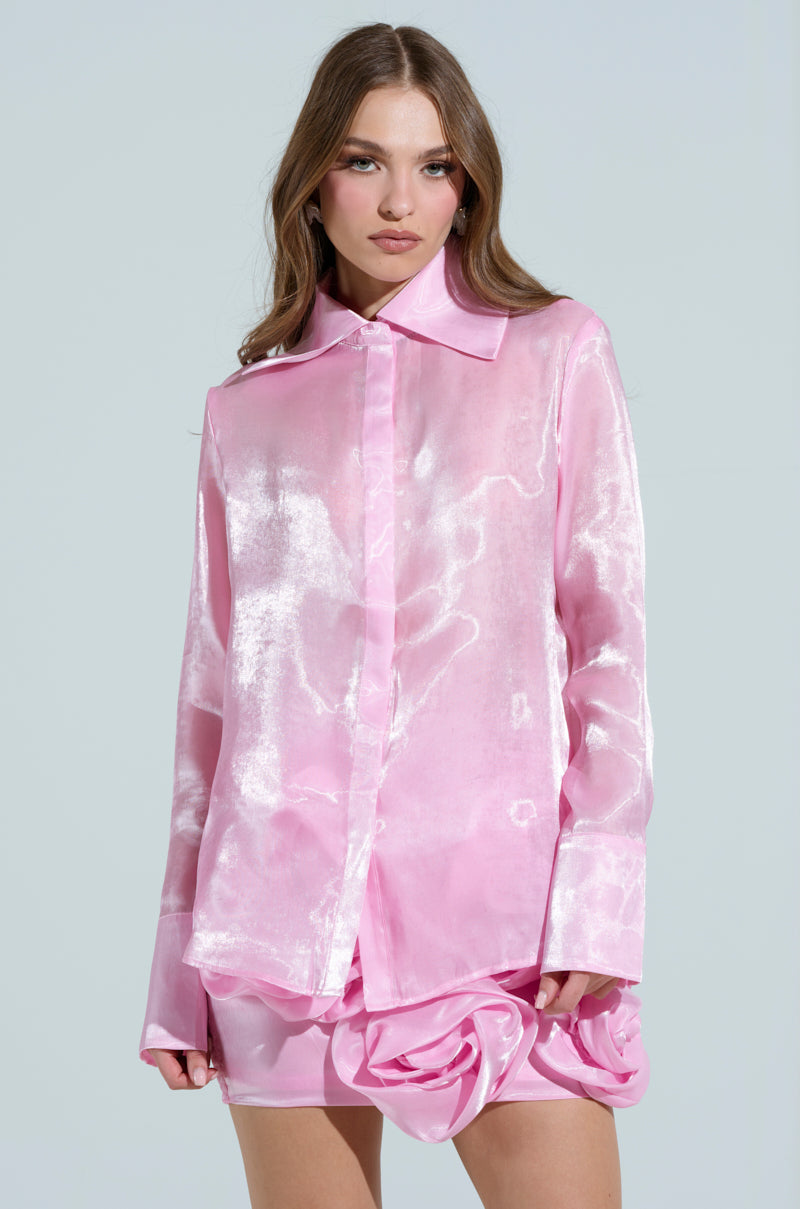 Against a plain background, someone with long hair wears the PRETTY HOT BUTTON DOWN TOP in shiny pink, featuring snap closures and a satin-like texture, matched with a coordinating skirt.