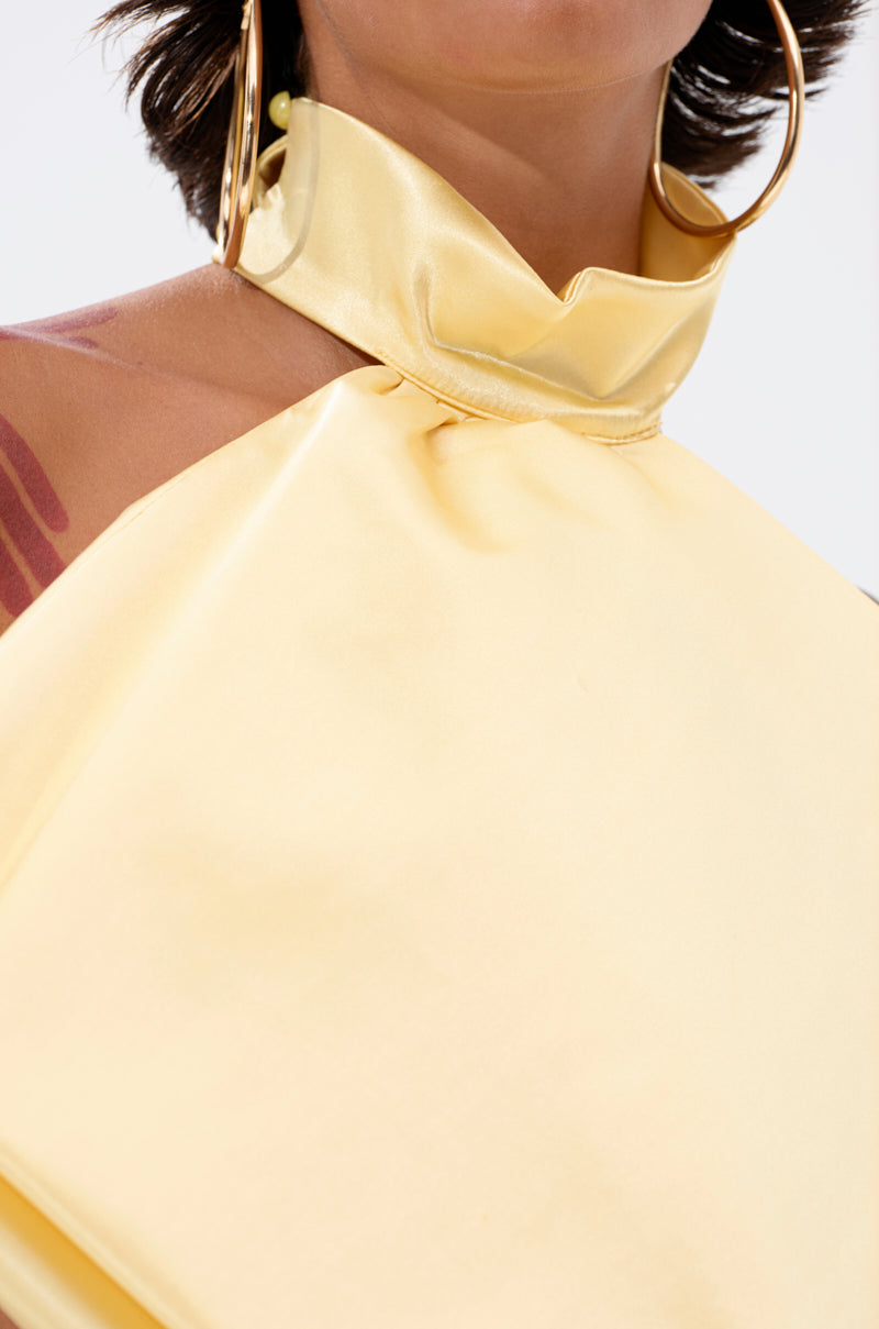 Close-up of a person wearing the KATE OVERSIZED NECKLACE, large gold hoop earrings, and a shiny pale yellow halter top with a high collar. A maroon tattoo is visible on their shoulder; only part of the face and upper body are shown.