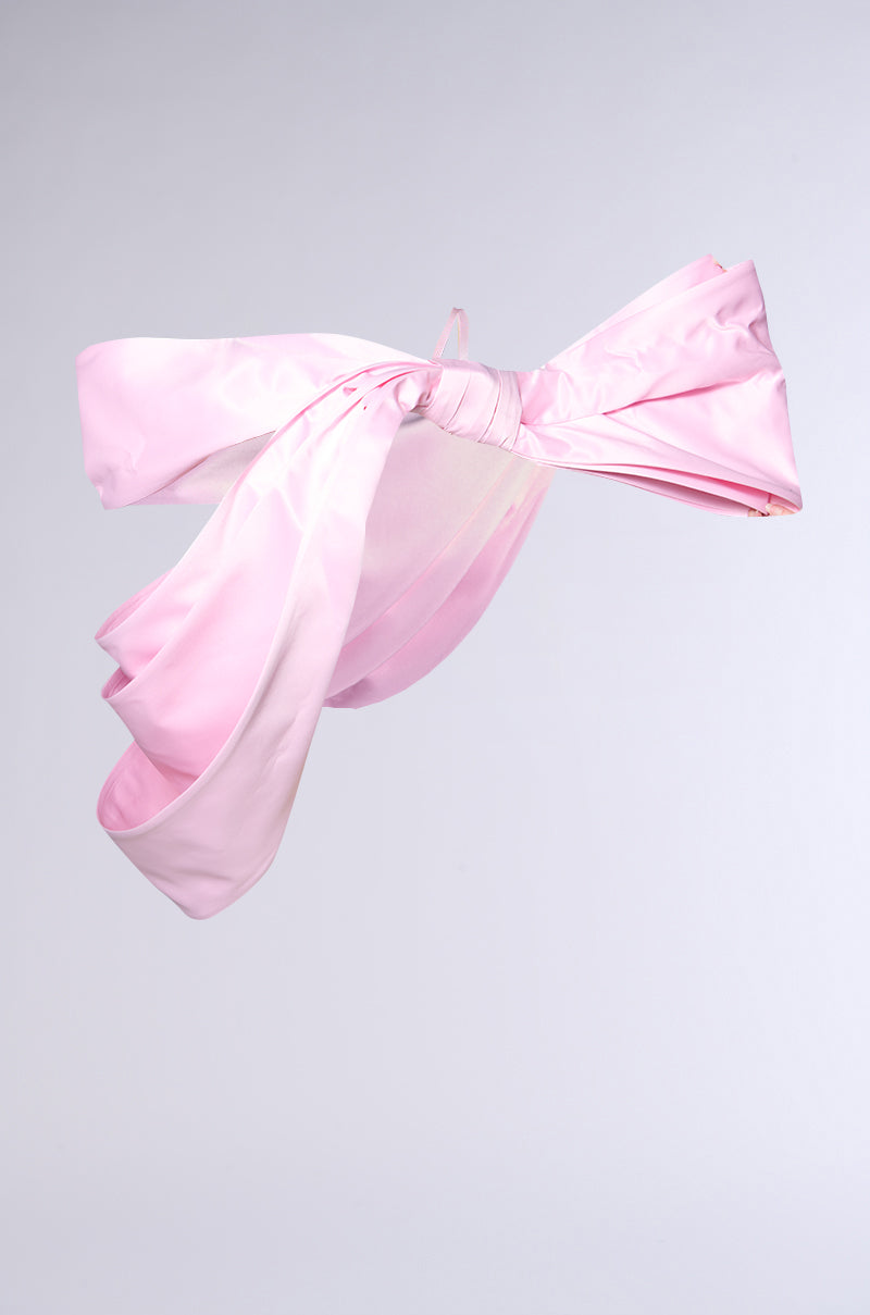The IM THE GIFT BODY ACCESSORY features a large, oversized pink satin bow with long, flowing tails, displayed against a plain light gray background for a bold, striking fashion statement.