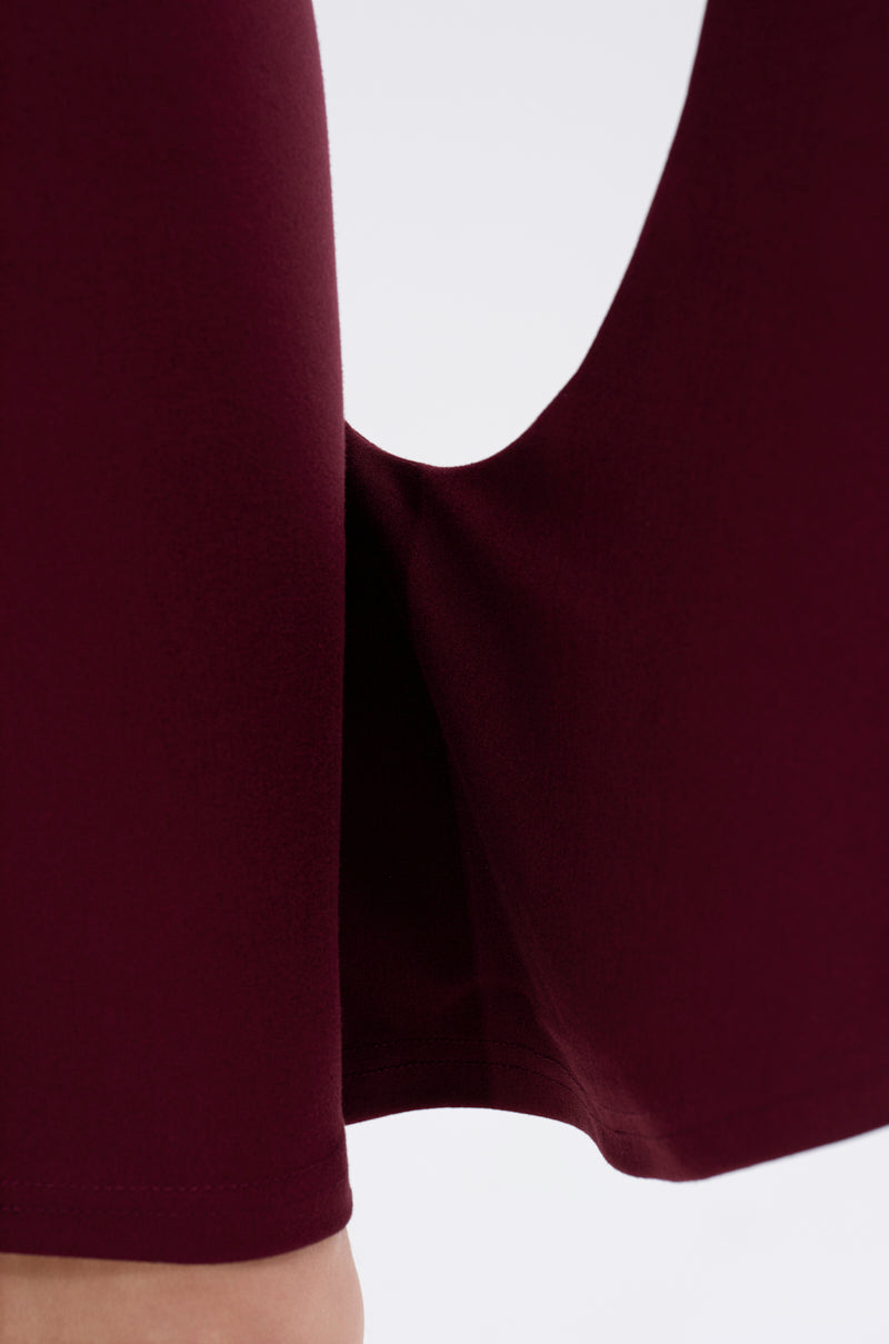 Close-up of the MEET ME IN THE BALLROOM MIDI DRESS IN BURGUNDY, featuring a maroon fabric pant leg with a high slit that reveals the ankle—ideal for formal events or styled with chic accessories against a light background.