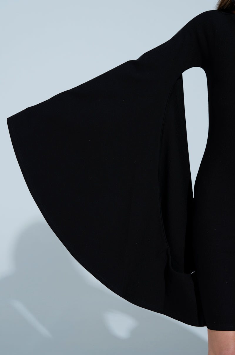 Someone wears the MEET ME IN THE BALLROOM MIDI DRESS, a black long-sleeved midi dress with wide bell sleeves and a boat neckline. The dress's dark fabric contrasts elegantly against a light blue background.