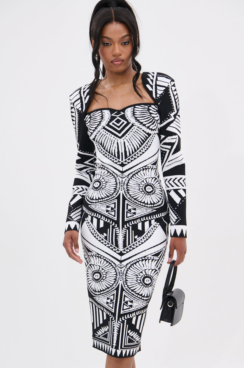 A woman in the NOT YOUR AVERAGE WOMAN PRINTED MIDI DRESS—a bold black and white geometric midi—holds a small black handbag and poses against a plain white background.