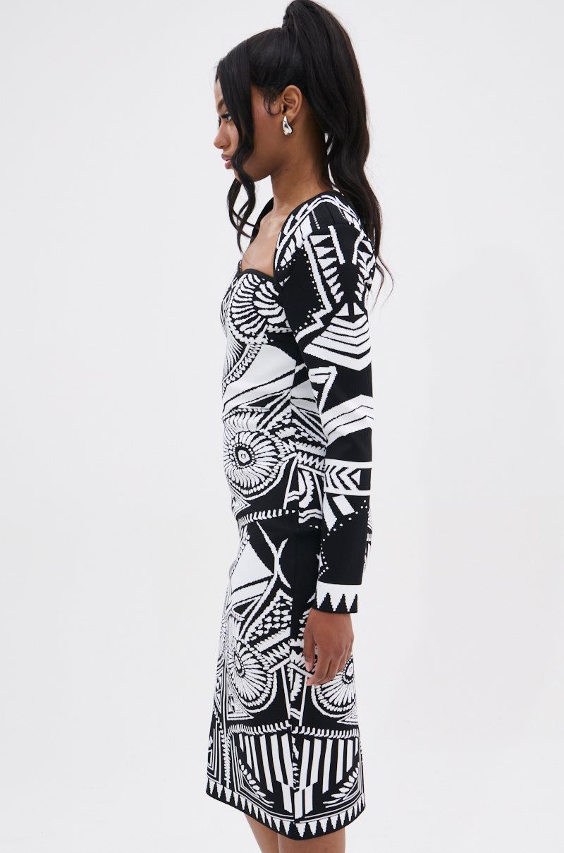 A woman with long dark hair in a ponytail wears the NOT YOUR AVERAGE WOMAN PRINTED MIDI DRESS in black and white, standing in profile against a plain white background.