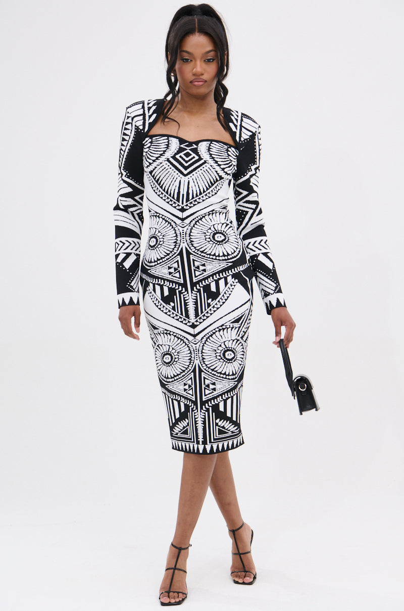 A woman in the NOT YOUR AVERAGE WOMAN PRINTED MIDI DRESS, featuring a black-and-white geometric pattern, long sleeves, and a square neckline, poses with a small black handbag against a white background.