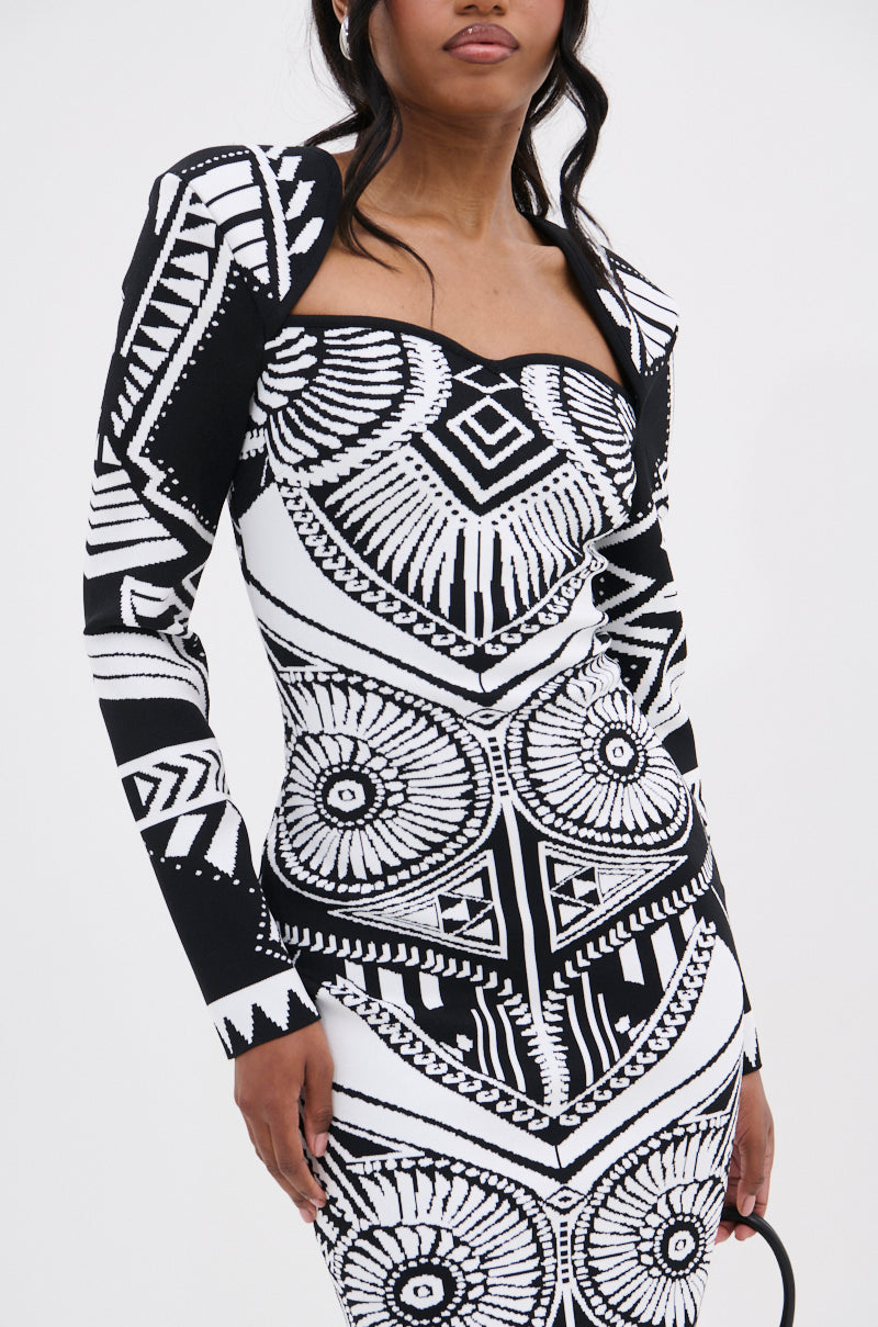 A woman models the NOT YOUR AVERAGE WOMAN PRINTED MIDI DRESS, a bold black and white midi with striking geometric circular and angular patterns, standing against a plain white background.