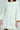 The person wears the LALA LOVE YOU SWEATER DRESS, showcasing a chunky off-white cable-knit style with wide sleeves and a ribbed collar. Its open weave adds cozy texture, while relaxed arms against a soft gray background enhance the garment's elegant design.