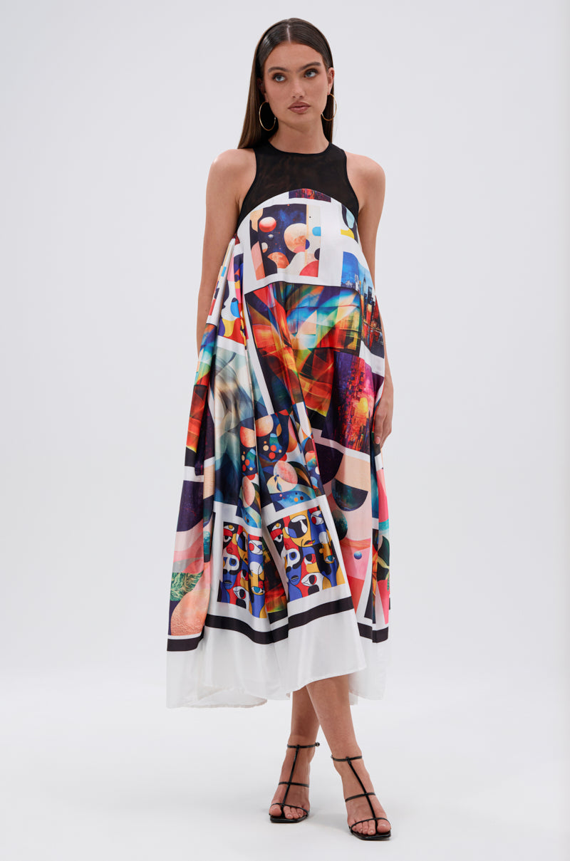 A woman with straight hair and strappy heels stands against a plain background, wearing the PUT ME IN A MUSEUM PRINTED MIDI DRESS—a sleeveless, high-neck midi dress featuring bold abstract graphics and an asymmetrical flowing hem.