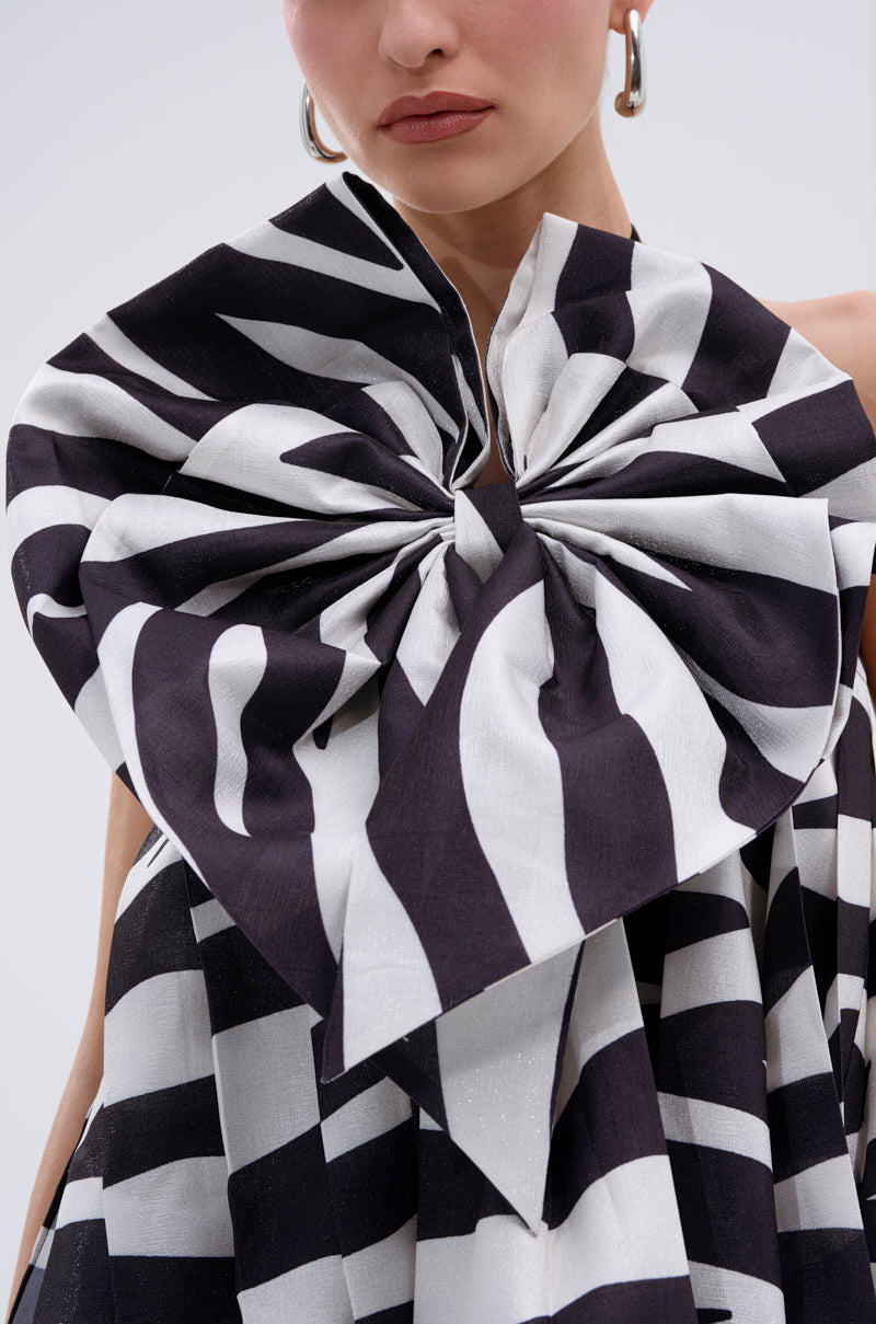 A woman wears large silver hoop earrings and the WILD THING BOW FRONT MINI DRESS with bold black-and-white stripes and a statement bow on the shoulder; only her lower face and upper chest are visible.
