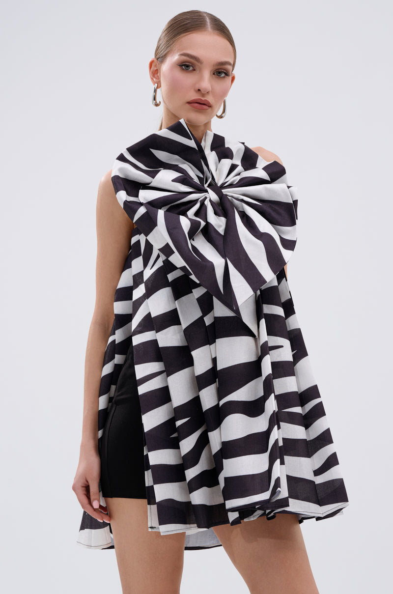 A woman stands against a white background wearing the WILD THING BOW FRONT MINI DRESS—black and white striped with an A-line silhouette—her hair pulled back and large hoop earrings completing the look.
