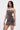 A woman with straight dark hair wears the ISLAND GIRL PRINTED MINI DRESS, a fitted mini dress with floral and abstract patterns. She holds a small silver purse and stands confidently against a plain white background.