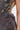 Close-up of a person wearing the ISLAND GIRL PRINTED MINI DRESS featuring glossy, dark fabric with nature-inspired patterns, side cut-out, and exposed back and waist. The background is plain and light-colored.