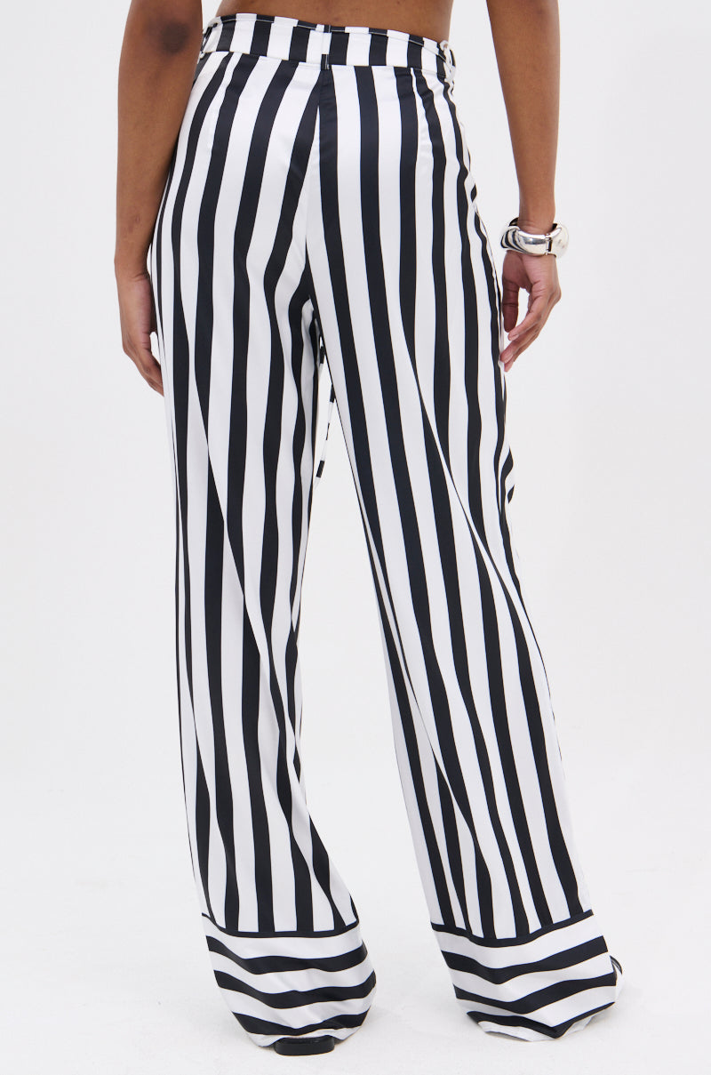 Only the lower back and legs are visible as someone stands against a plain white background, wearing BEETLE JUICE VIBES SATIN PANTS with a high-rise fit, wide-leg cut, and bold black-and-white stripes.