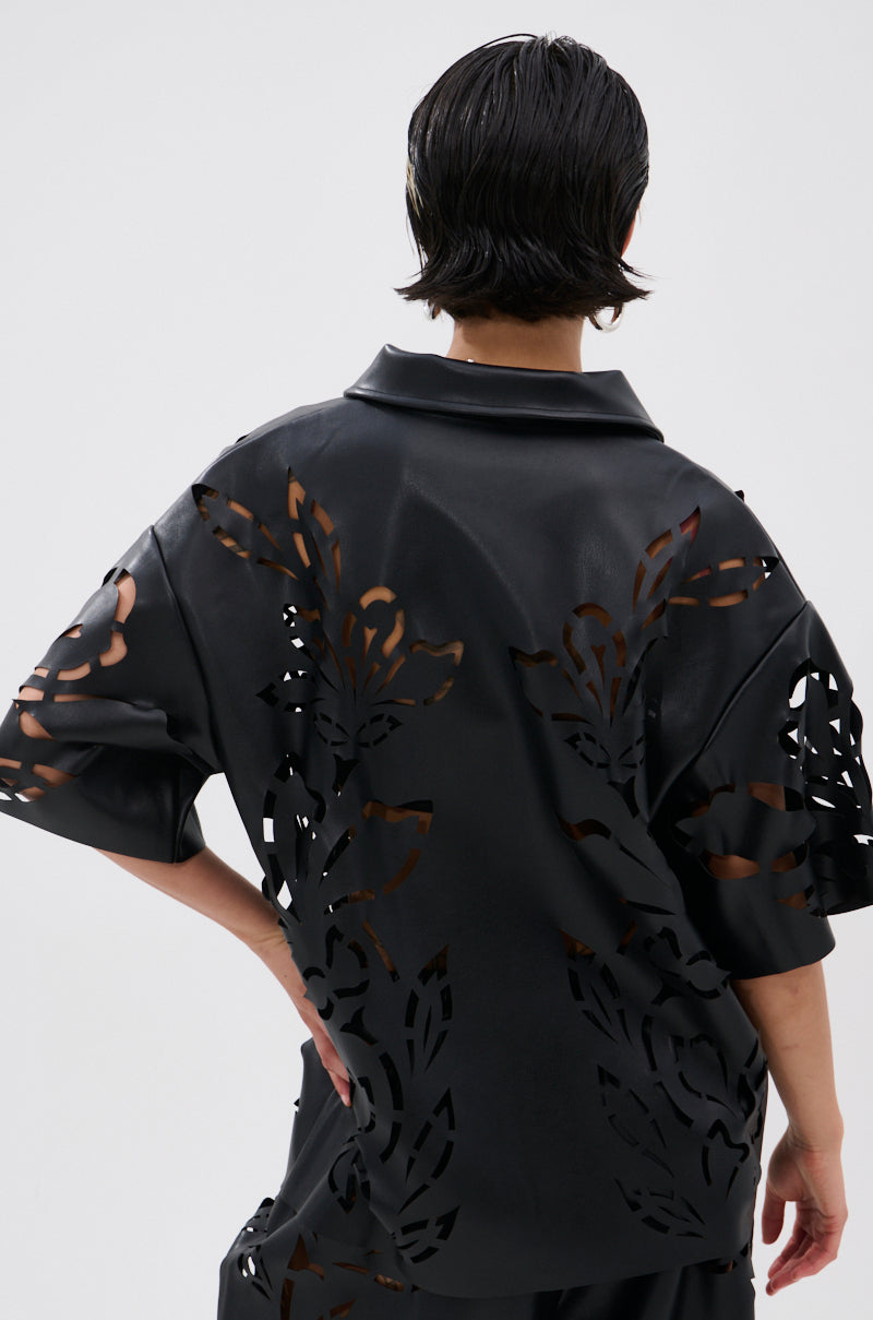 Seen from behind, a person with short, wet-look hair wears the GOING CRAZY PU CUTOUT BUTTON DOWN TOP—black, short-sleeved, featuring bold floral cutouts—against a plain light background.