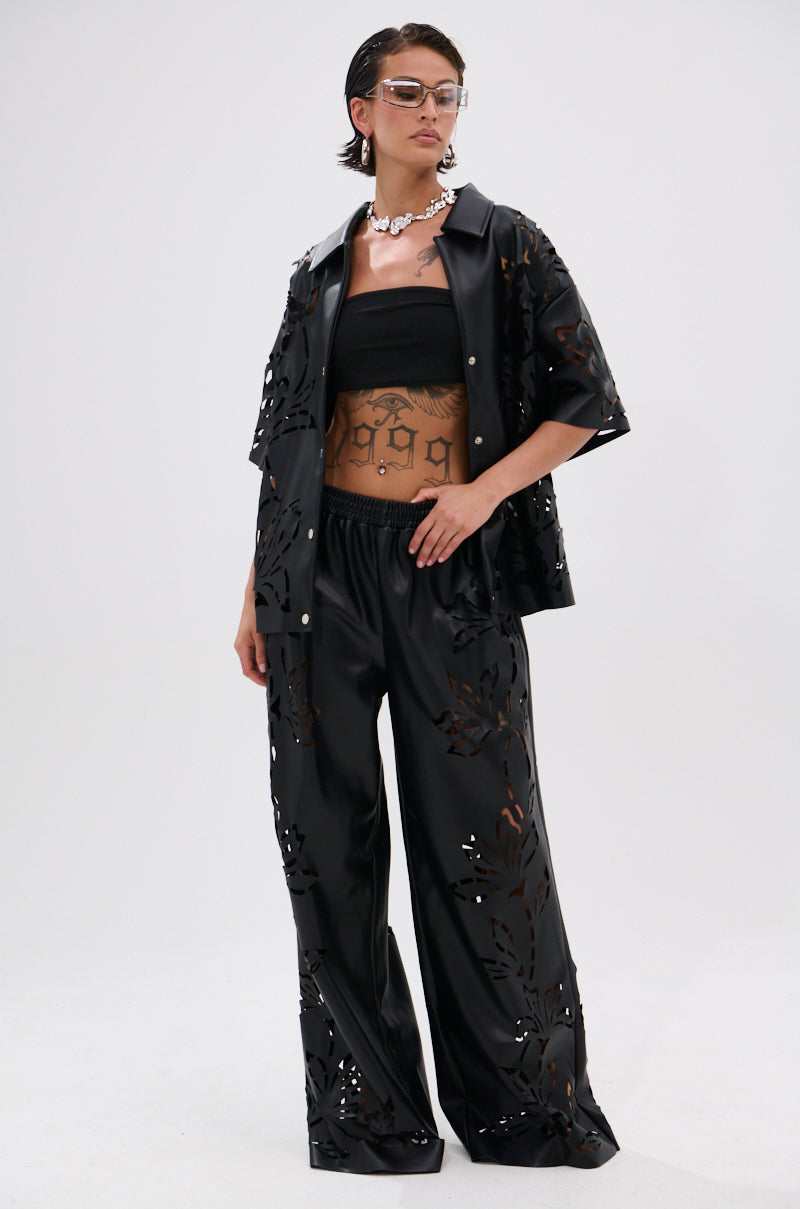 Wearing the GOING CRAZY PU CUTOUT BUTTON DOWN TOP and loose black cutout pants, paired with a matching open short-sleeve jacket. The oversized look is finished with clear glasses, a chunky necklace, and visible tattoos.