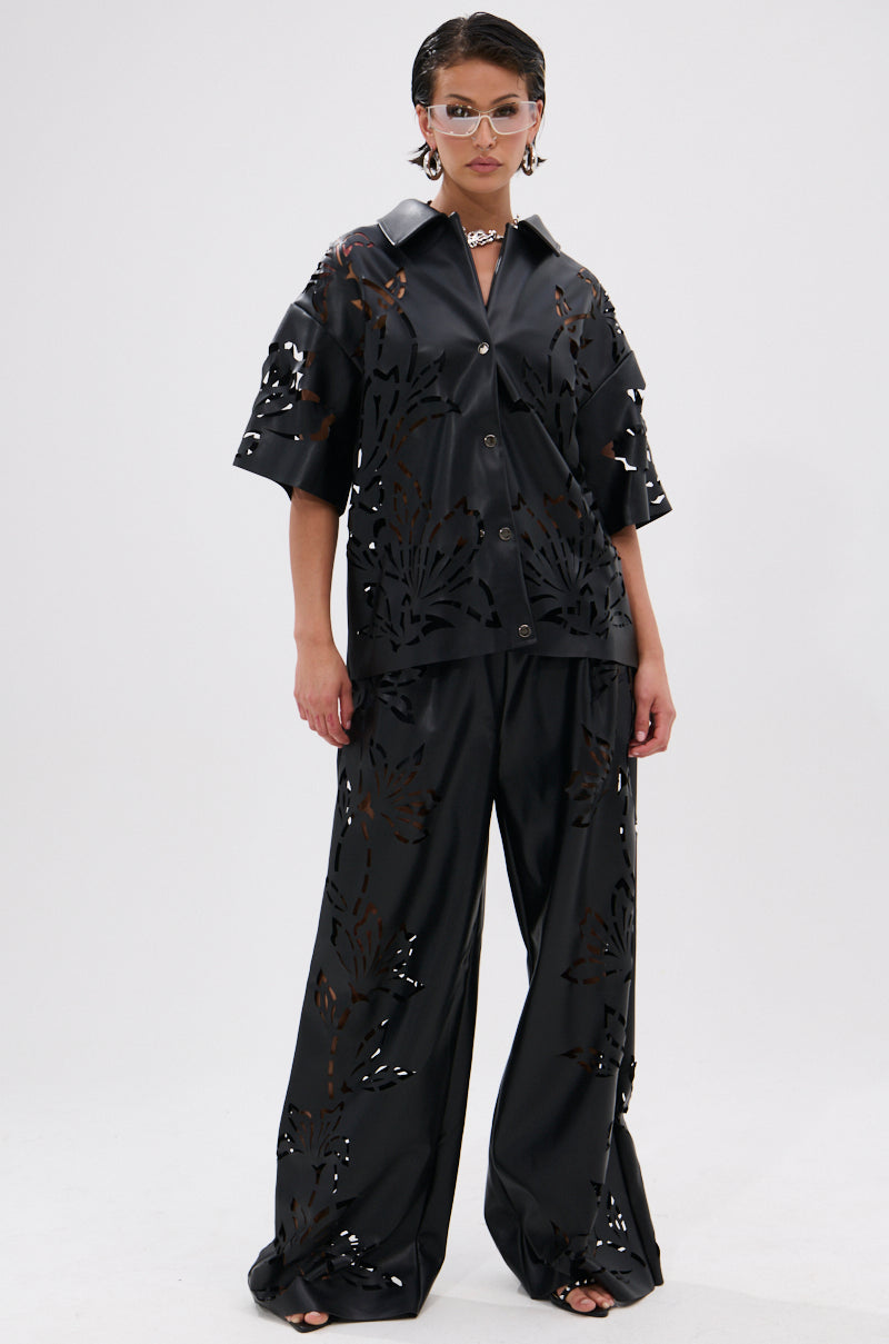 Wearing the GOING CRAZY PU CUTOUT BUTTON DOWN TOP in black with cut-out details, paired with wide-leg pants, sunglasses, a choker necklace, and slicked-back hair for a bold, edgy look.