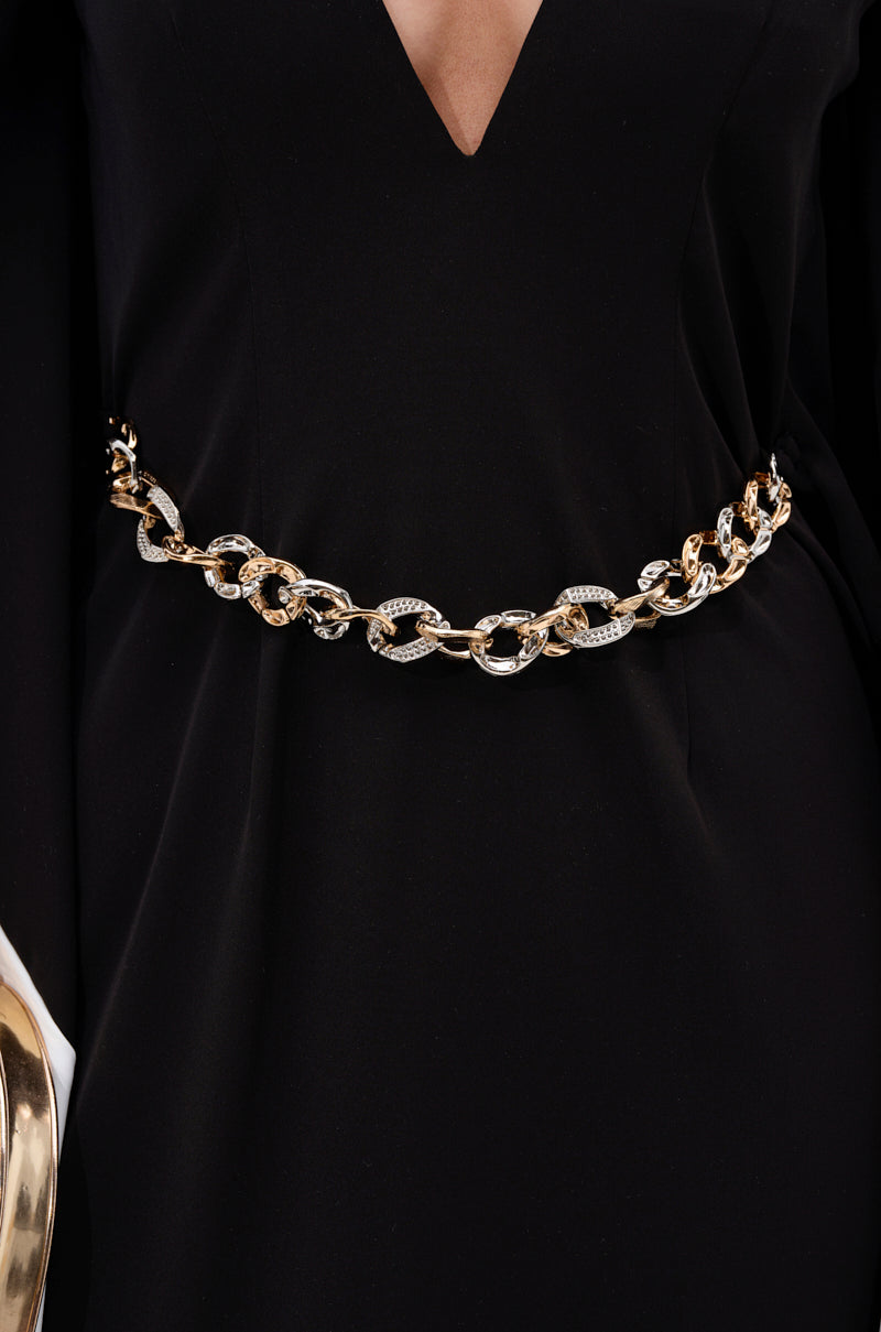 A person wearing the JULIE TWO TONE MIDI DRESS featuring a black color block design and deep V neckline, accessorized with a chunky gold and silver chain belt at the waist.