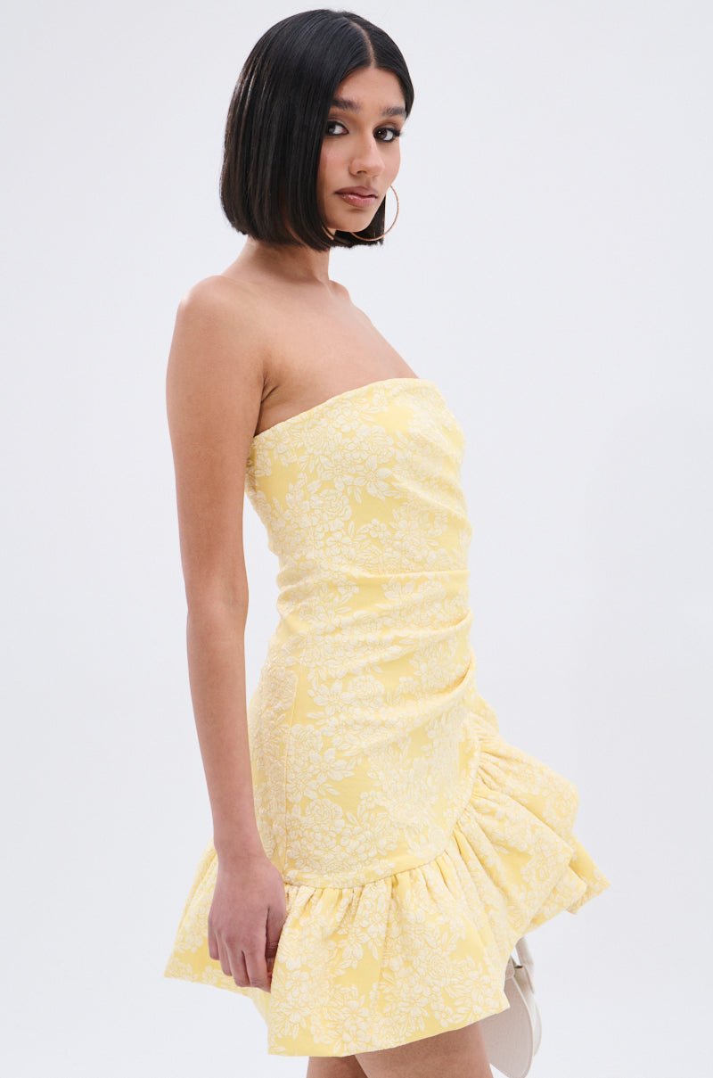 A woman with a sleek bob wears the GARDEN PARTY MINI DRESS, featuring a ruched bodice, white floral print, and ruffled hem, standing against a plain white background.