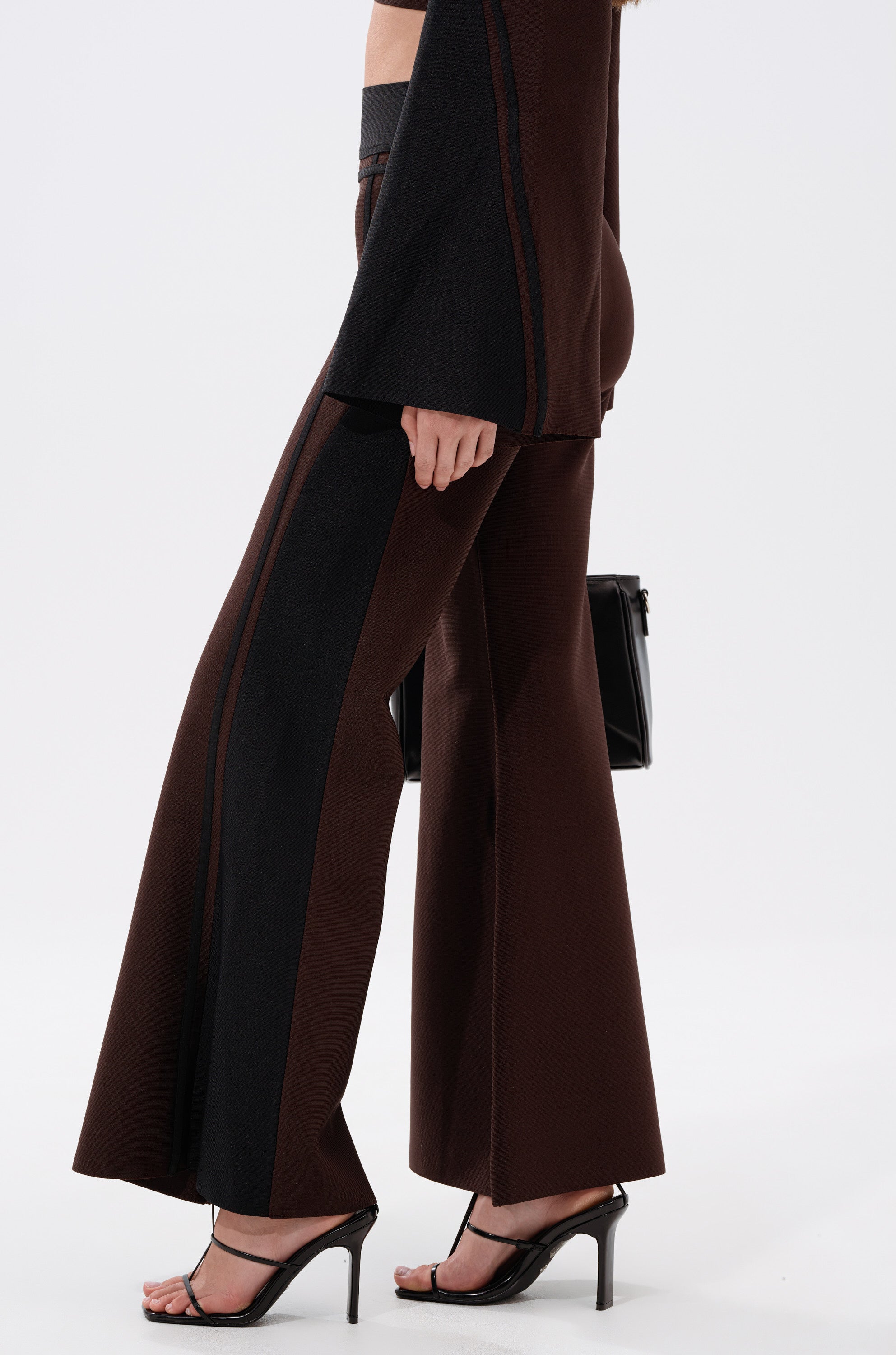 A person stands against a plain white background wearing the MAZIE WIDE LEG PALAZZO PANT in brown and black, a matching jacket, black heeled sandals, and holding a black handbag.