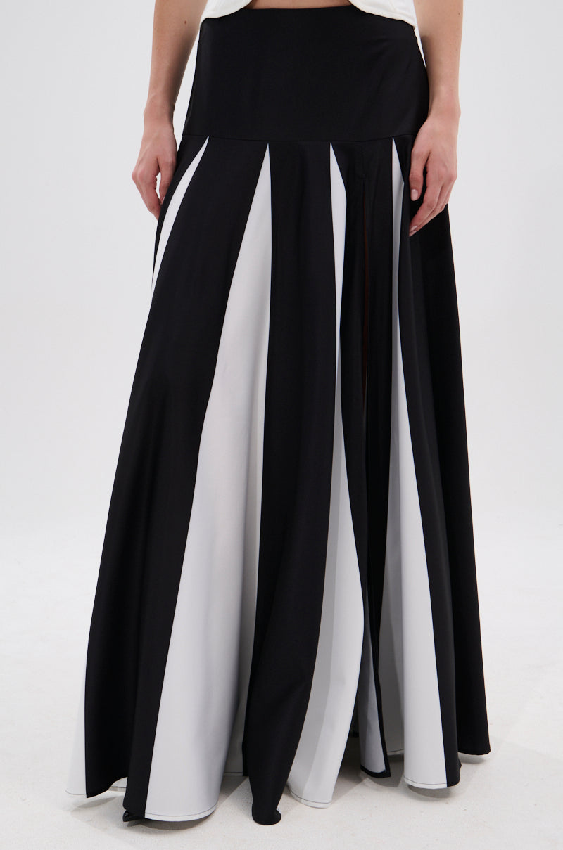 A person models the RACHEL SATIN MAXI SKIRT, featuring alternating black and white vertical panels and a high-rise waistband. The lower half of the body is shown against a plain white background with hands resting by their sides. 2