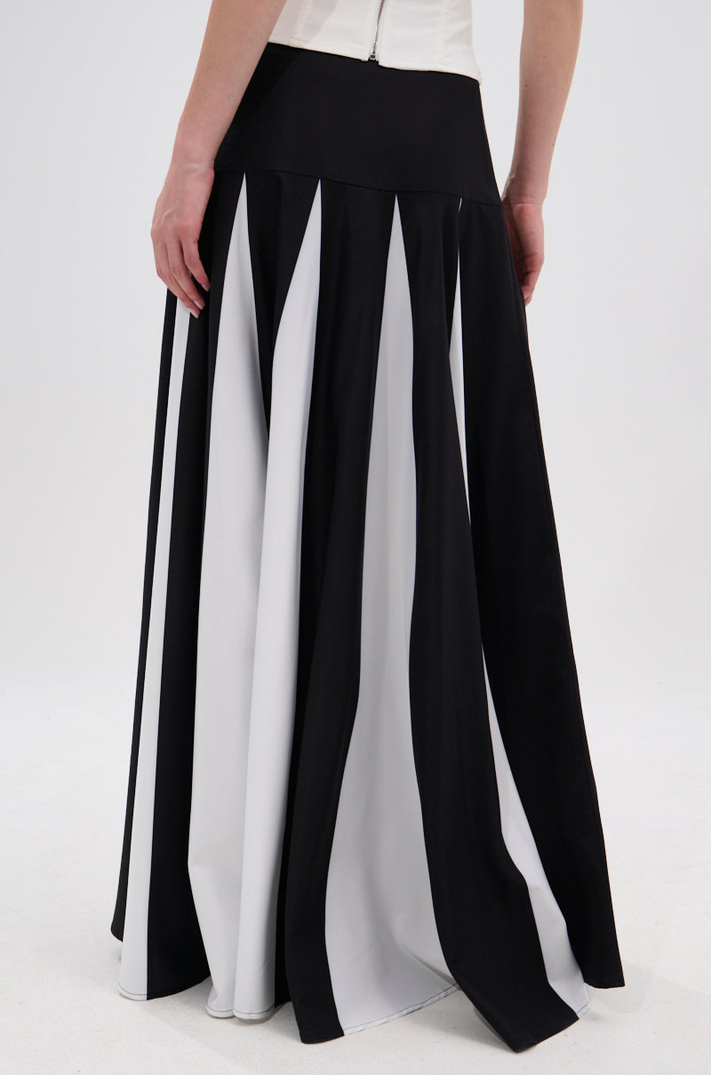 A person wears the RACHEL SATIN MAXI SKIRT, shown from the back. The flared, flowing monochrome design has alternating black and white panels and a high-rise waistband, while their arm rests naturally at their side. 5
