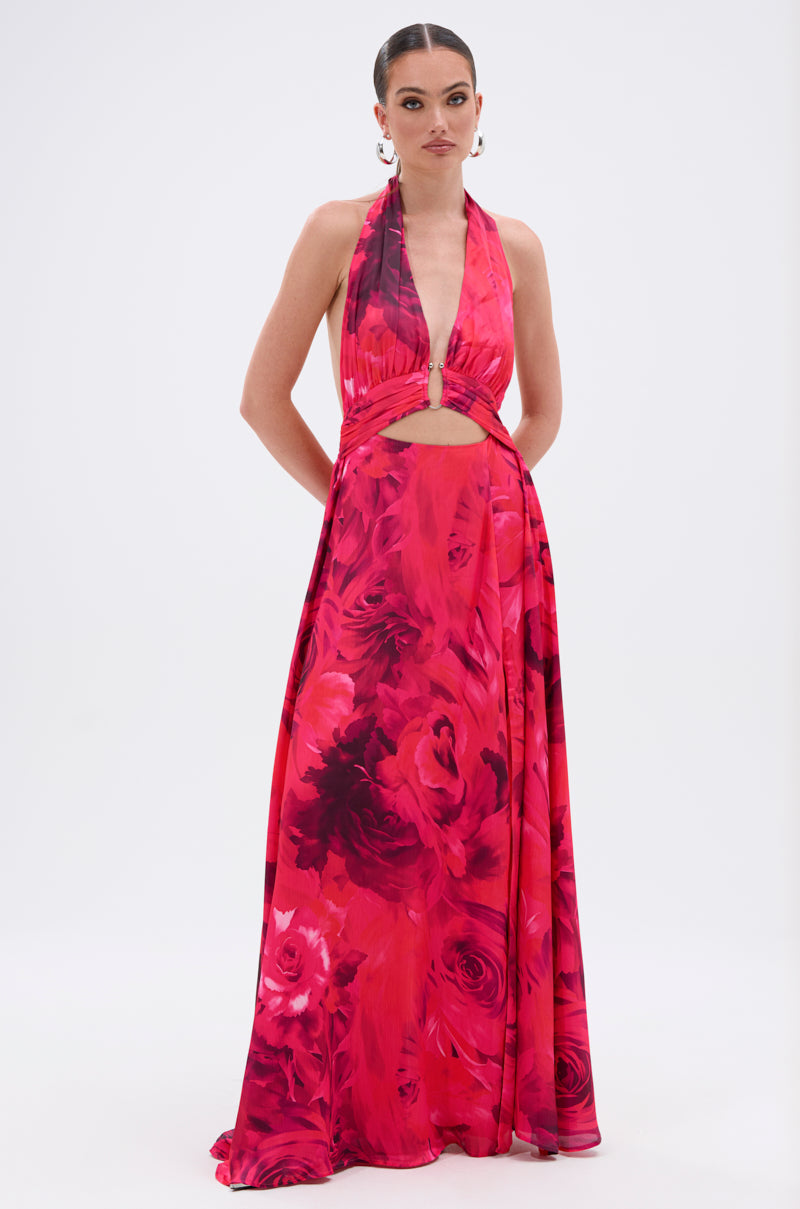 A woman models the ALL EYES ON ME CUT OUT MAXI DRESS, featuring a vibrant floral print, deep V-neck, sleeveless cut, and bold red and pink flowers against a plain white background.