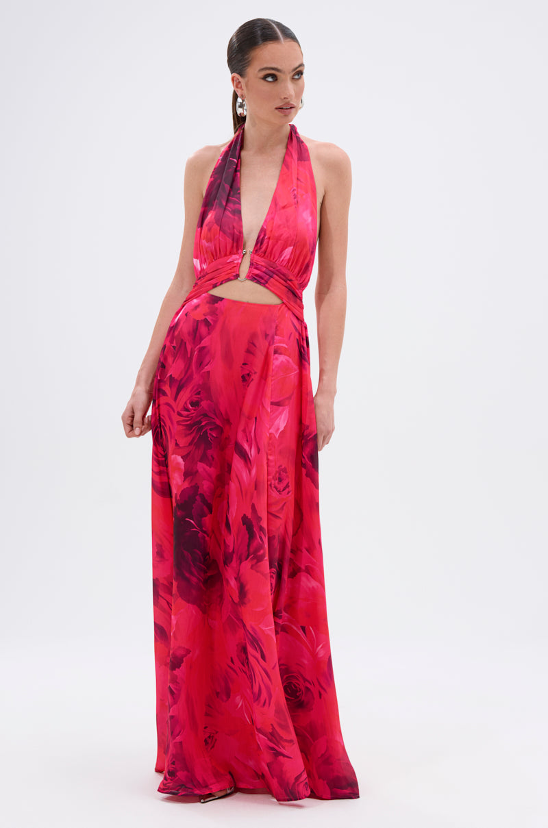 A woman models the ALL EYES ON ME CUT OUT MAXI DRESS, a sleeveless halter-style dress featuring a red and pink floral print and front cut-out detail, set against a plain white background.