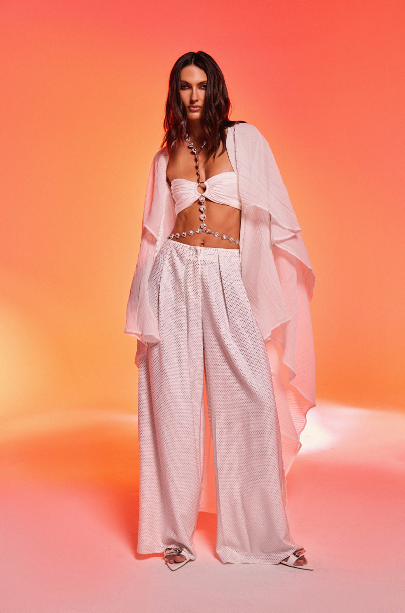 A woman strikes a pose in the FLY AWAY WITH ME BLOUSE IN WHITE, highlighting the chic elegance of this longline blouse.