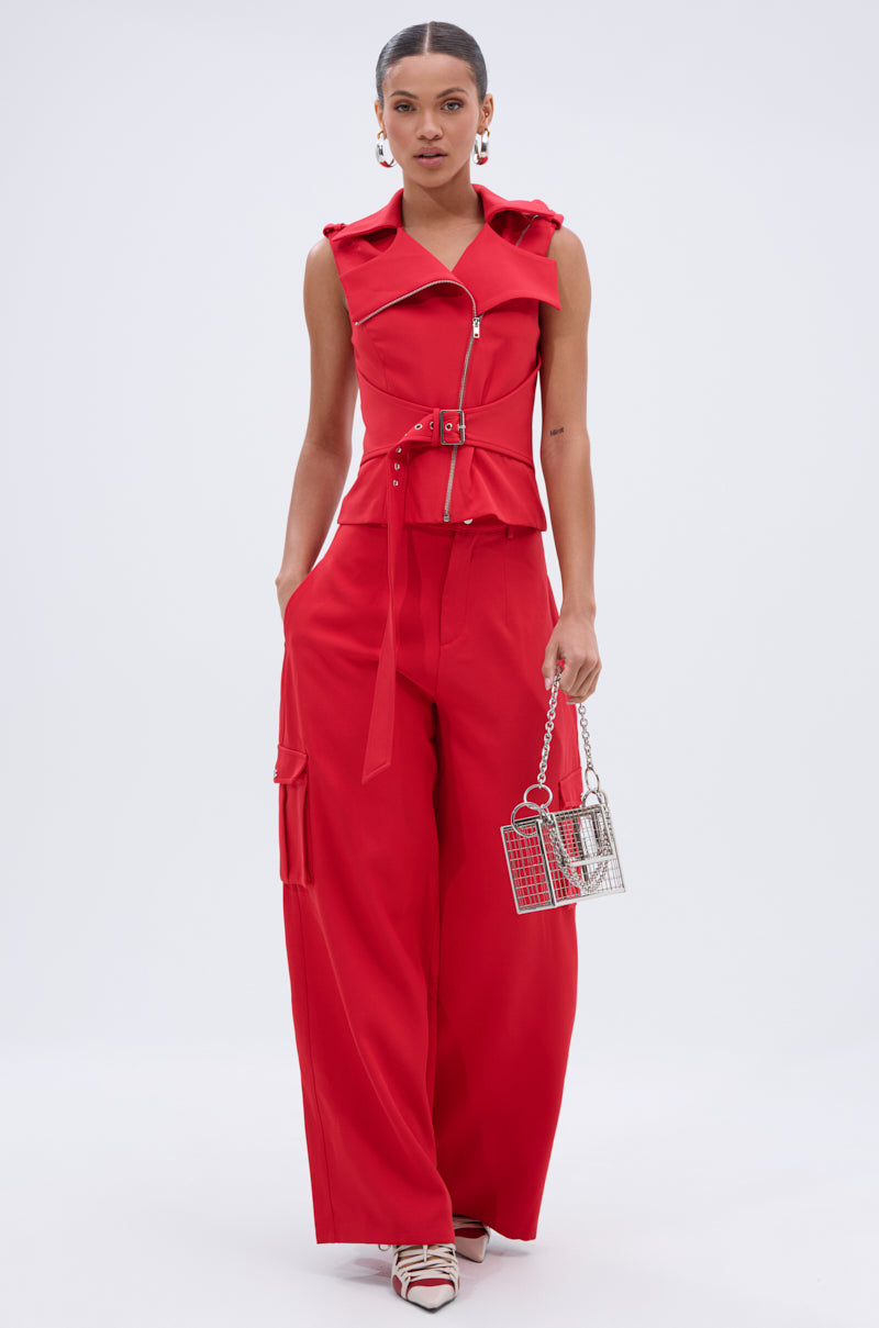 A woman poses against a plain background, wearing the LAURA MOTO VEST in chic red with a belted waist and wide-leg pants. She pairs it with a metallic handbag, hoop earrings, and strappy pointed heels for a stylish look. 5