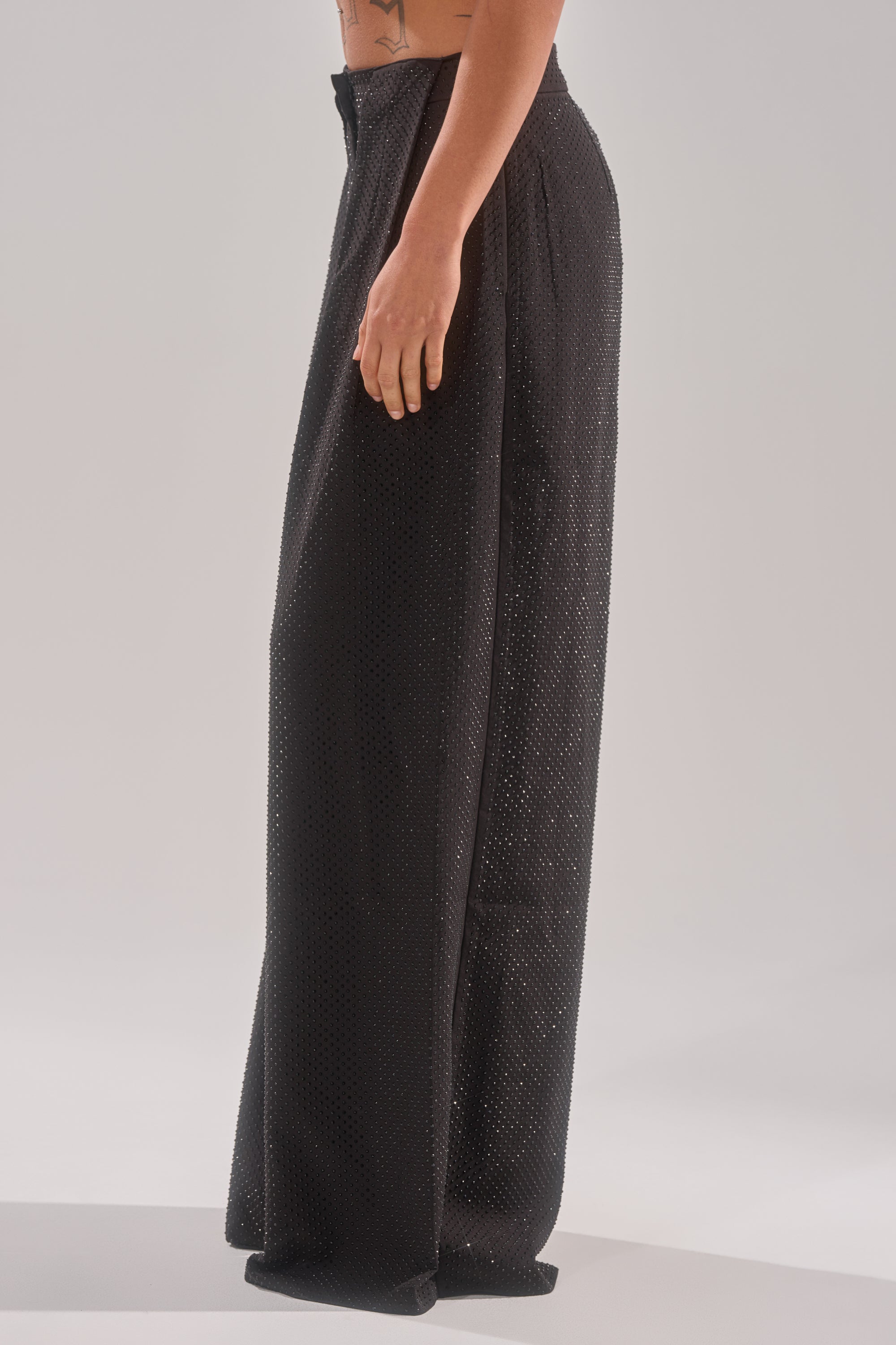 A person stands sideways against a plain light background, showing only their lower torso and legs in the SPARKLE QUEEN TROUSER—loose-fitting, high-waisted wide-leg pants with a subtle sparkle pattern. 3