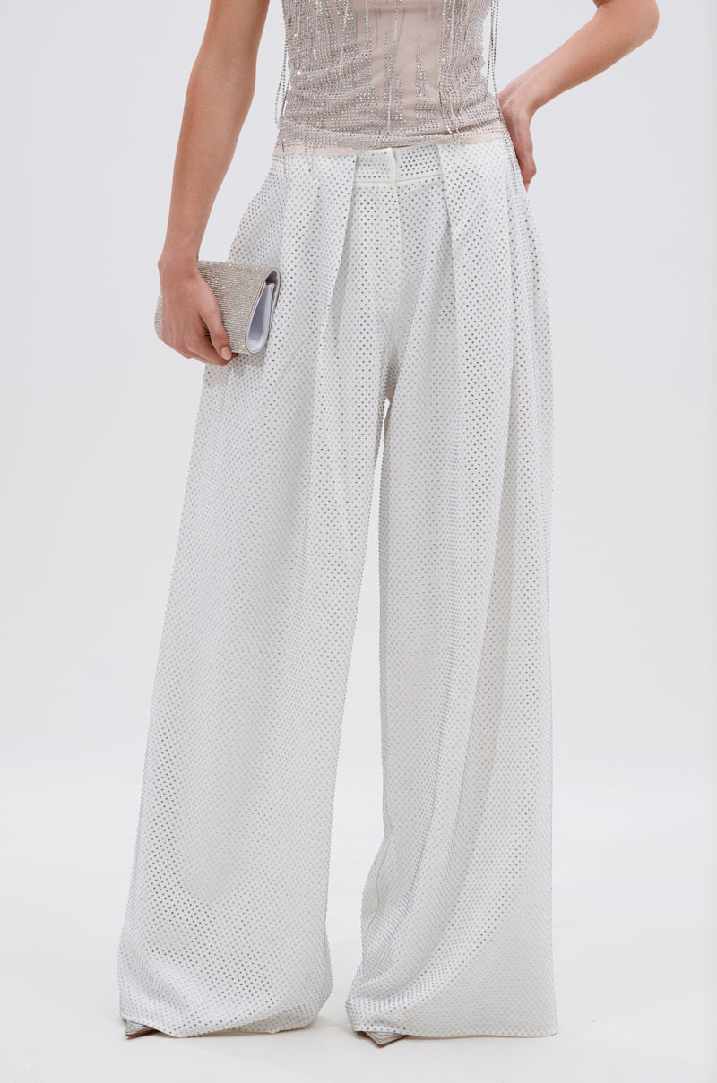 A person wears the SPARKLE QUEEN TROUSER with a wide-leg, high-waist, pleated light-textured fabric, holding a metallic clutch. Shown waist down against a plain white background.