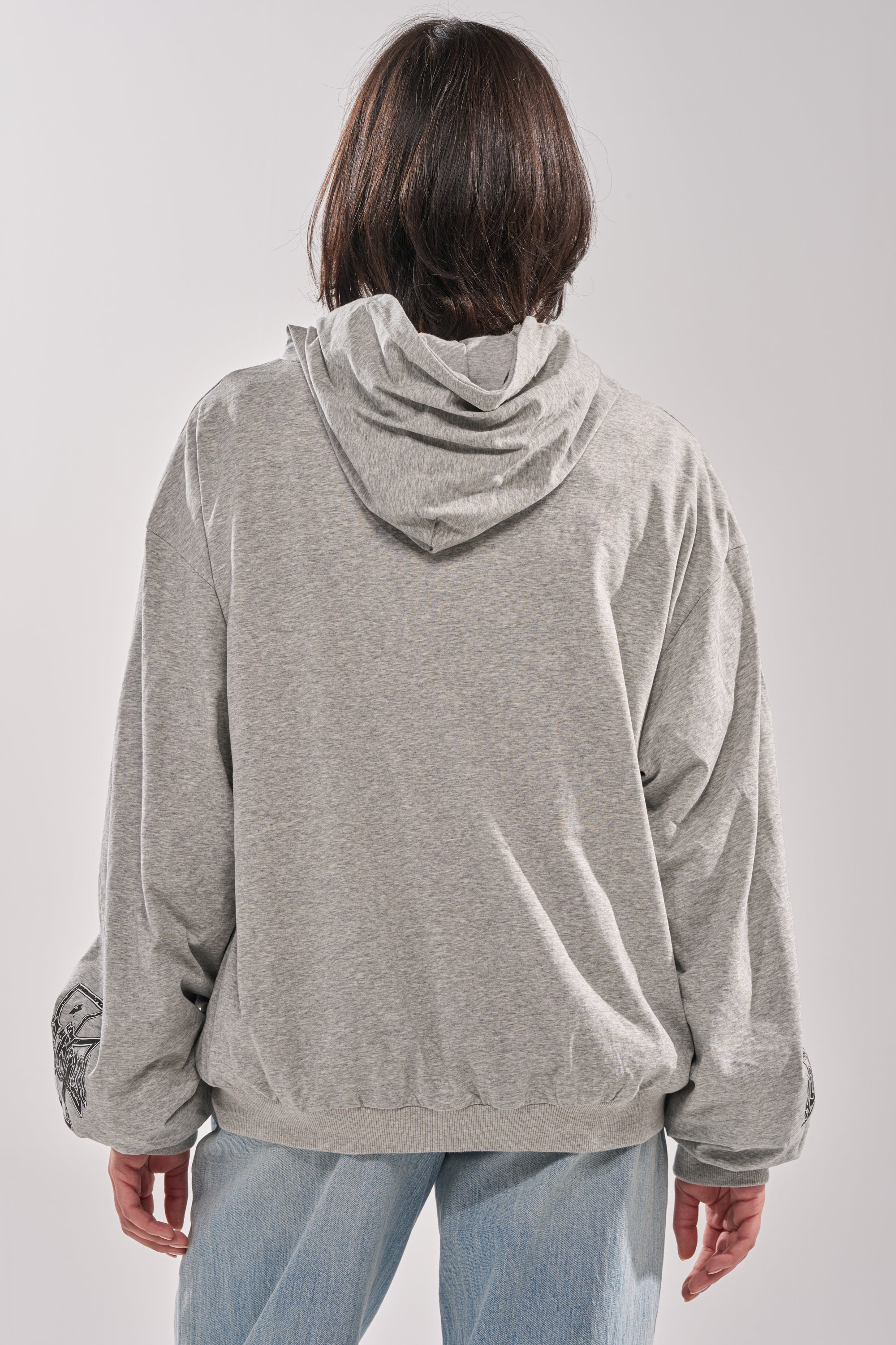 A person with shoulder-length dark hair stands with their back to the camera, wearing the EPIC REVERSIBLE ZIP UP SWEATSHIRT and light blue jeans against a plain background. 12