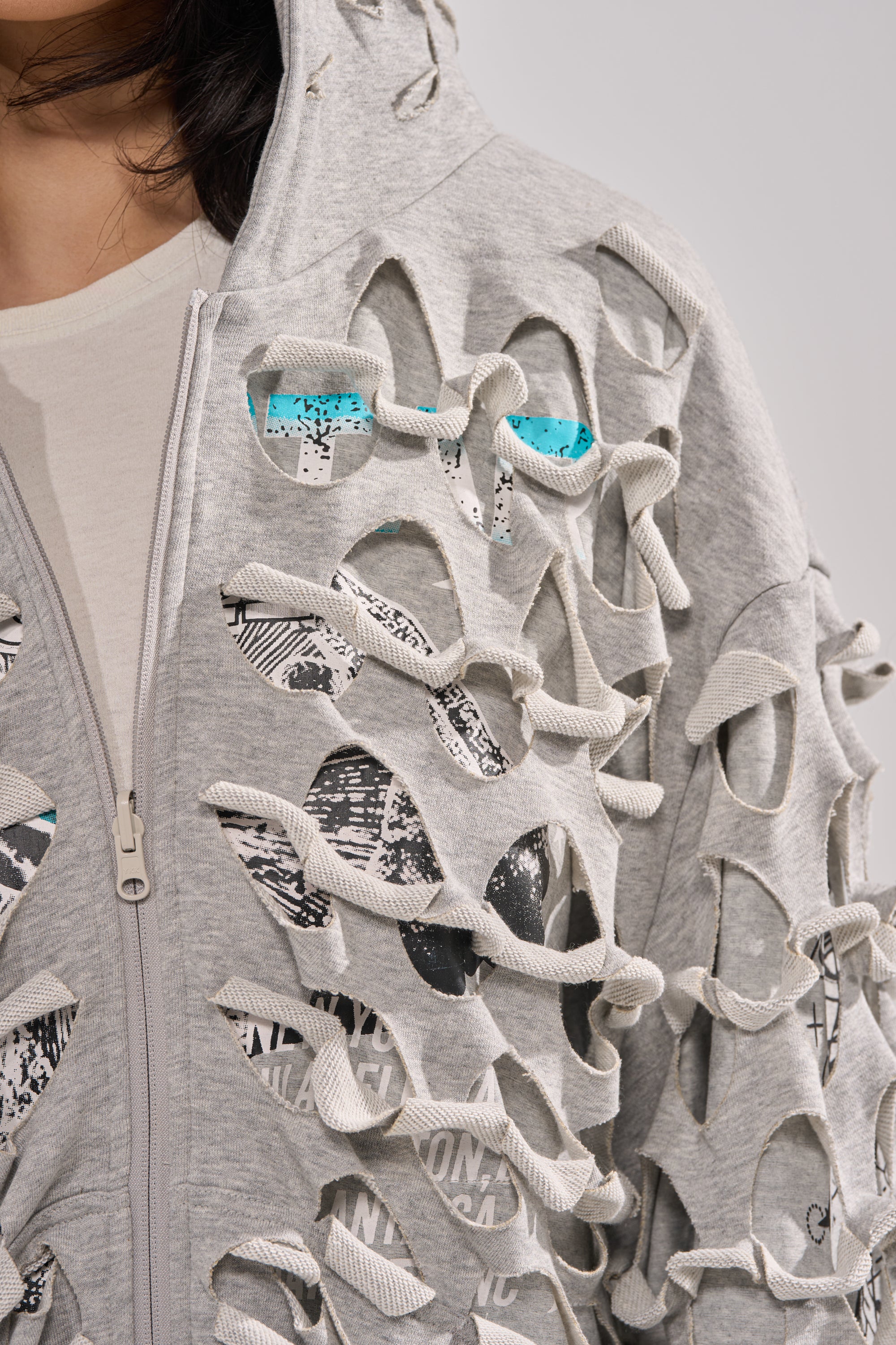 A close-up of a person wearing the EPIC REVERSIBLE ZIP UP SWEATSHIRT featuring large oval cutouts and knot details, revealing a black, white, and teal patterned shirt underneath for a modern streetwear look. 17