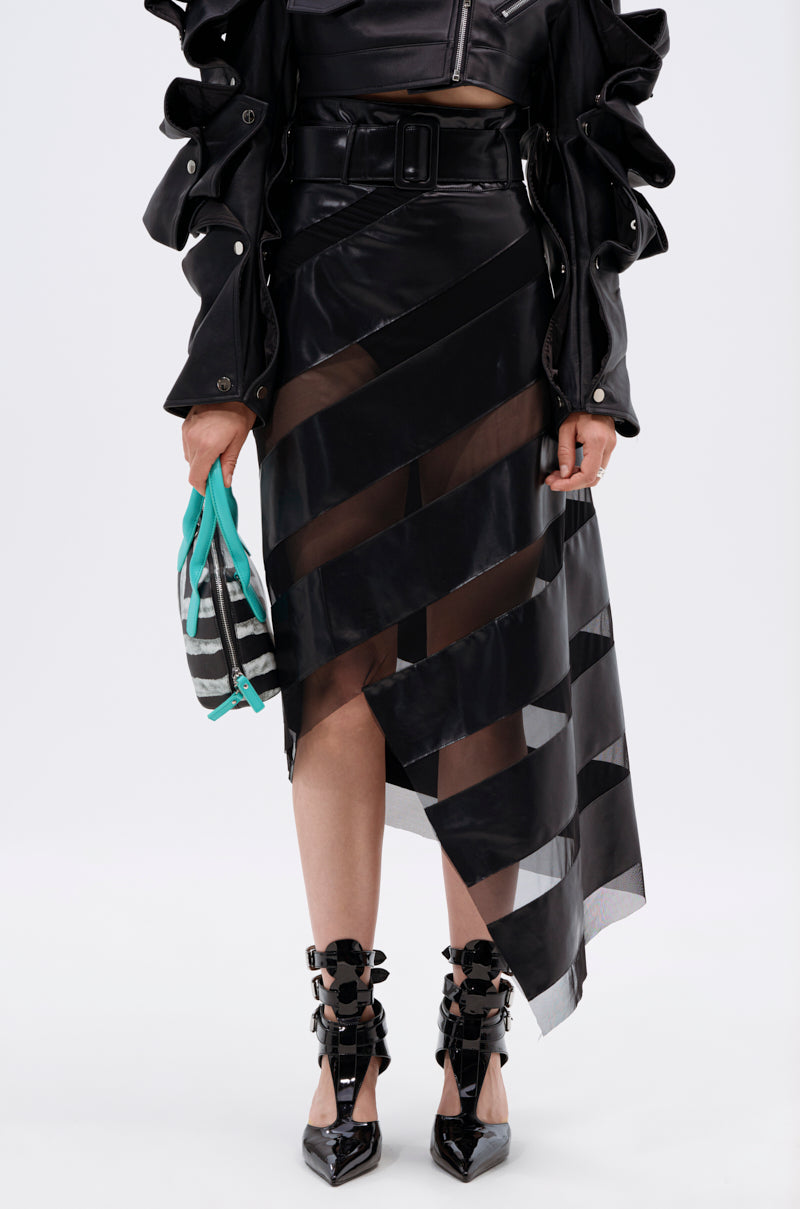 A person wears a black leather outfit with ruffled sleeves and the SOMETHING DIFFERENT MESH MIDI SKIRT WITH FAUX LEATHER, featuring sheer diagonal stripes, plus a small turquoise-and-black bag and black pointed bow high heels.