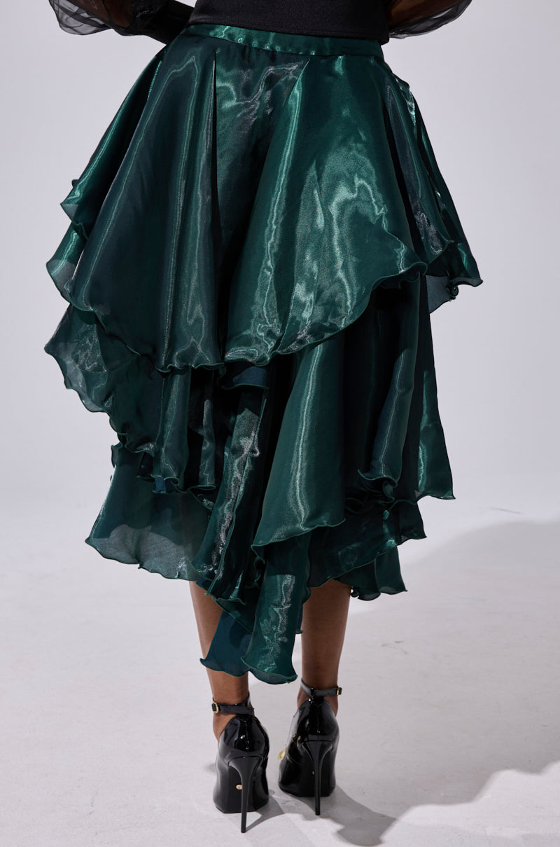 A person wears the LUXE LIFE SATIN MIDI SKIRT in shiny dark green with black high-heeled shoes, standing on a light floor against a plain background. 4