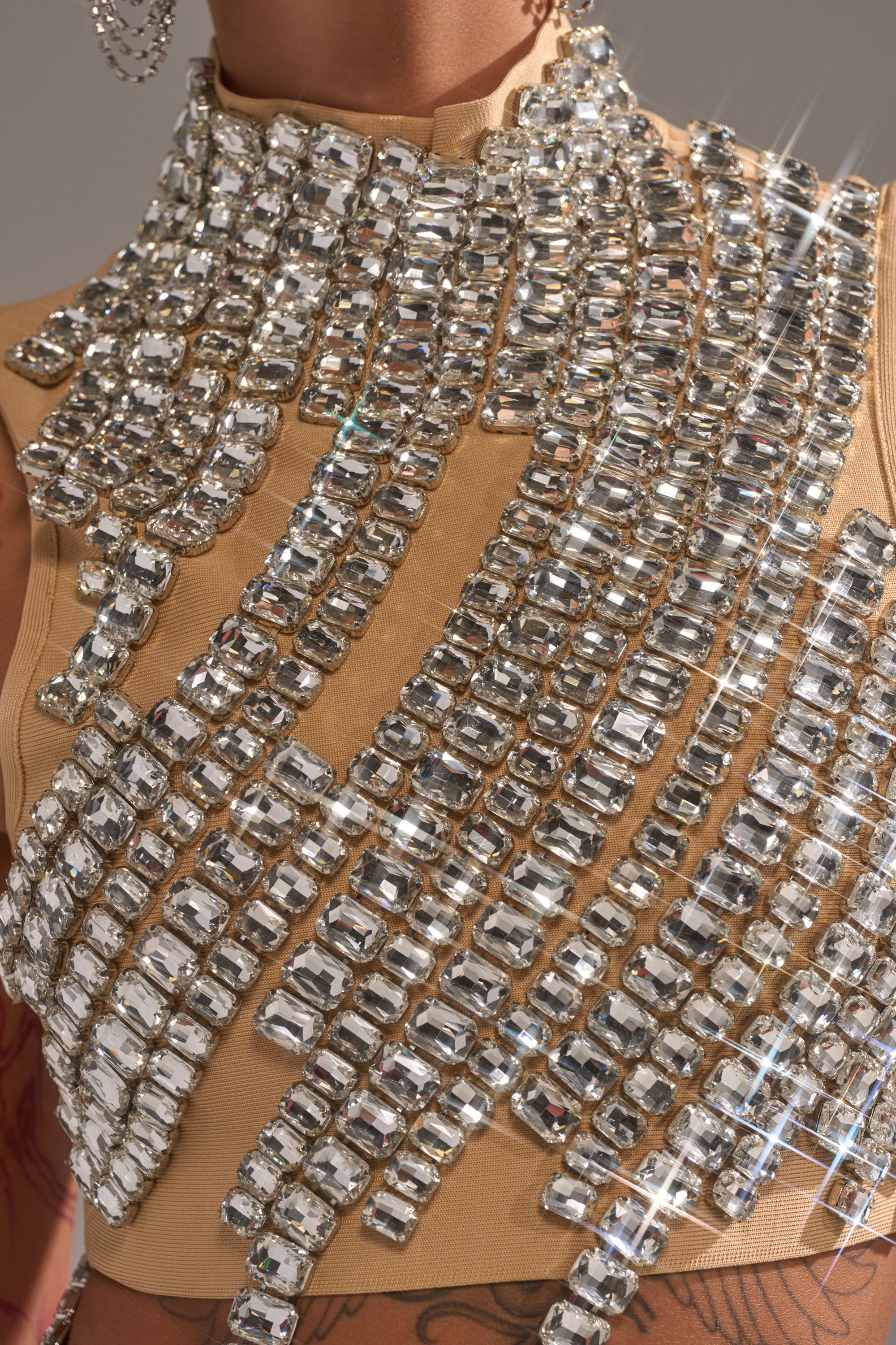 A close-up of the ITS YOUR TIME RHINESTONE MOCK NECK BLOUSE in beige, featuring sleeveless bandage fabric with sparkling rectangular rhinestones in diagonal rows for a dazzling effect.