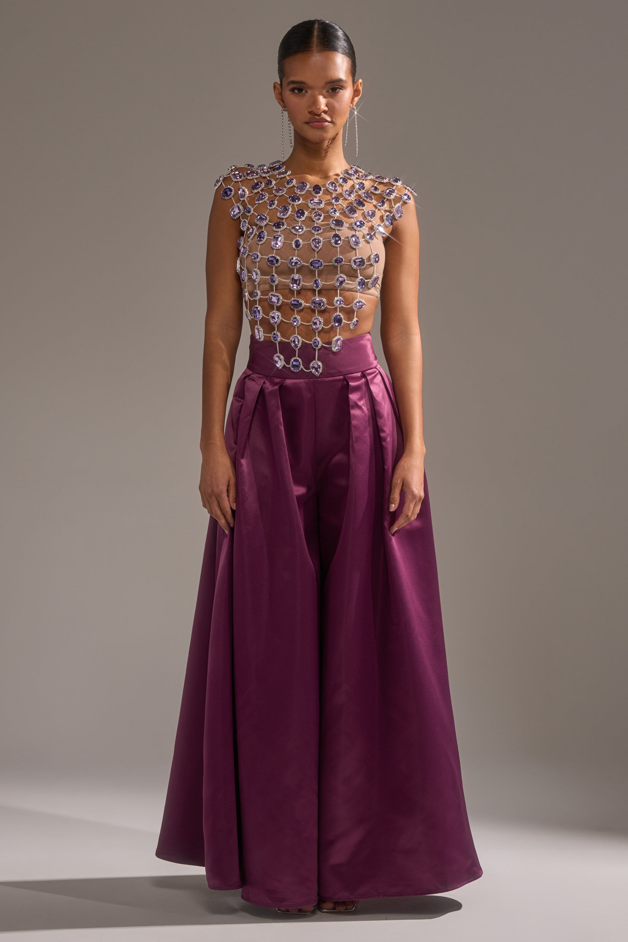 A woman models the LOVER GIRL RHINESTONE CHAIN TOP—crystal-embellished in a chain pattern—paired with wide-legged, high-waisted deep magenta satin pants and slicked-back hair for a striking statement look. 8