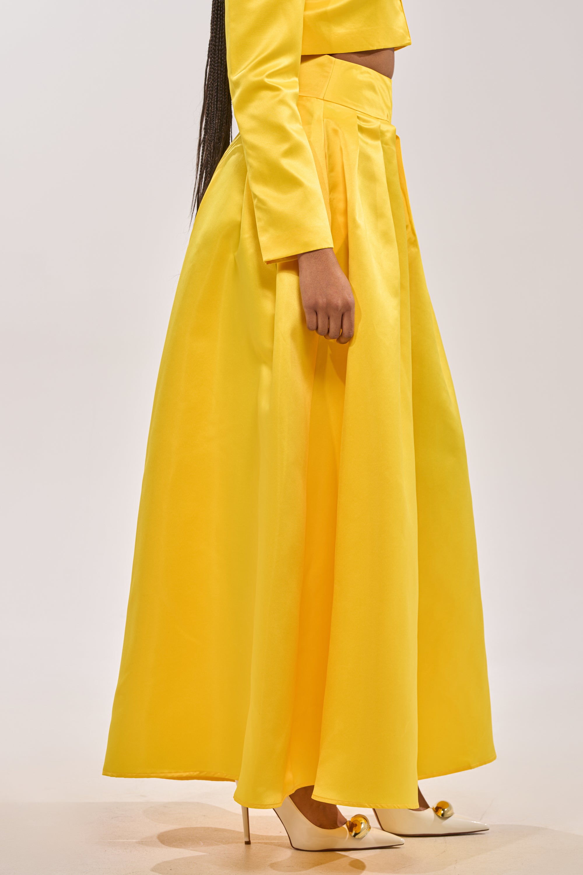 A person wears the BLOOMING WIDE LEG TROUSER in yellow satin with a matching long-sleeve top and white high heels with gold accents, set against a plain light background. 2