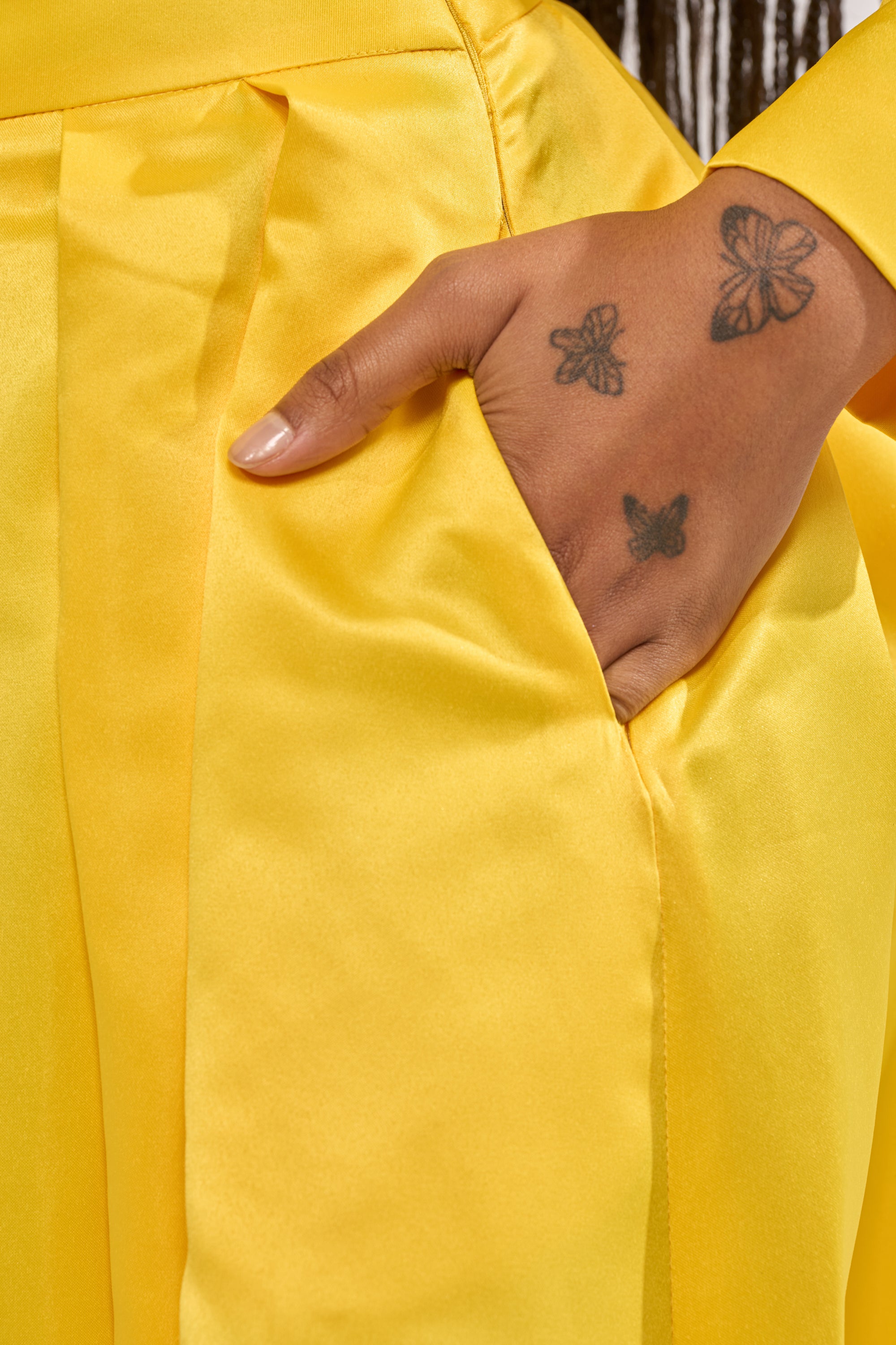 A close-up of a tattooed hand resting in the pocket of bright yellow BLOOMING WIDE LEG TROUSER. 6