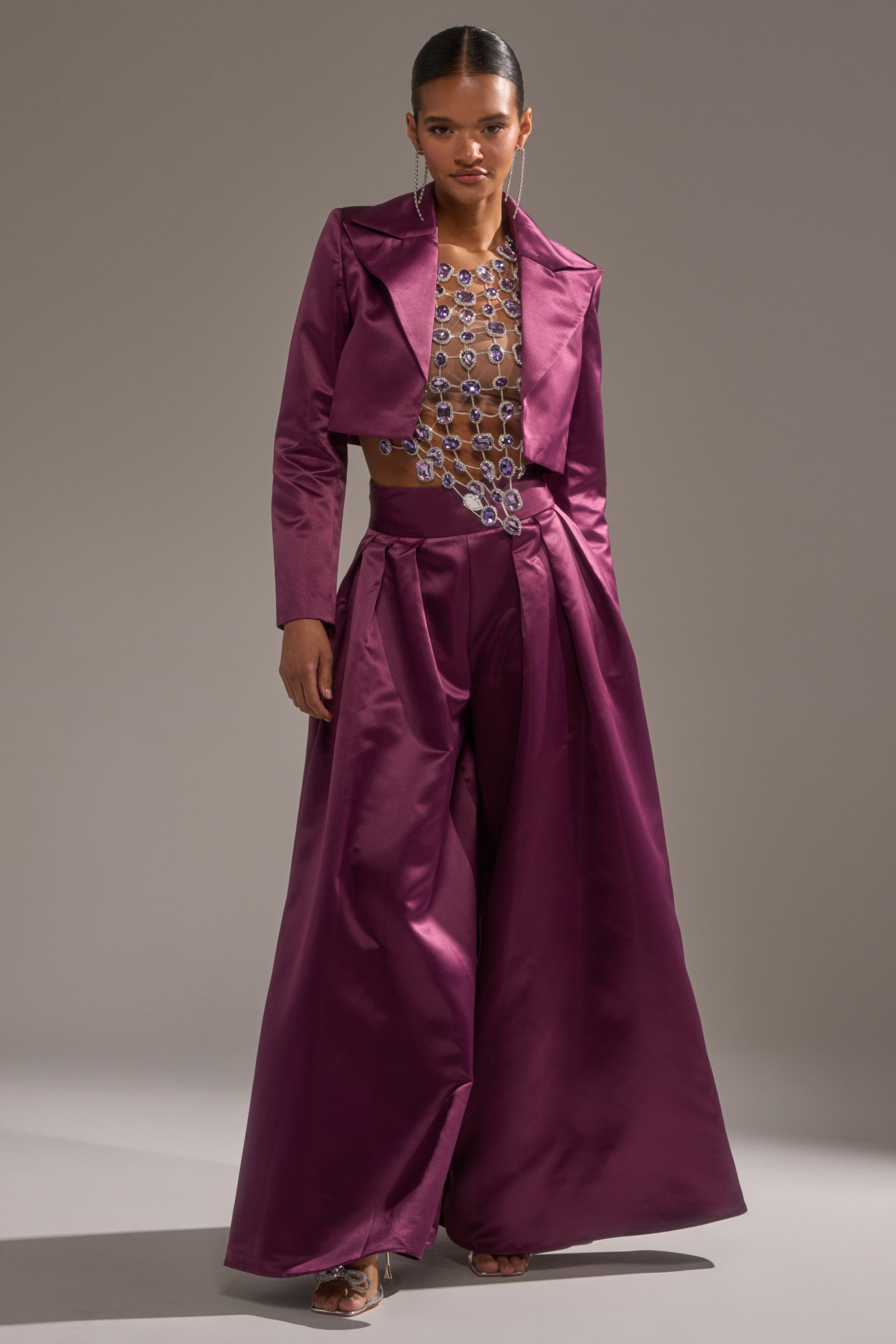 A model wears the ON AND ON WIDE LEG TROUSER in shiny magenta, featuring a high-rise fit and wide legs, paired with a cropped jacket and a crystal-embellished sheer top, set against a plain light background.