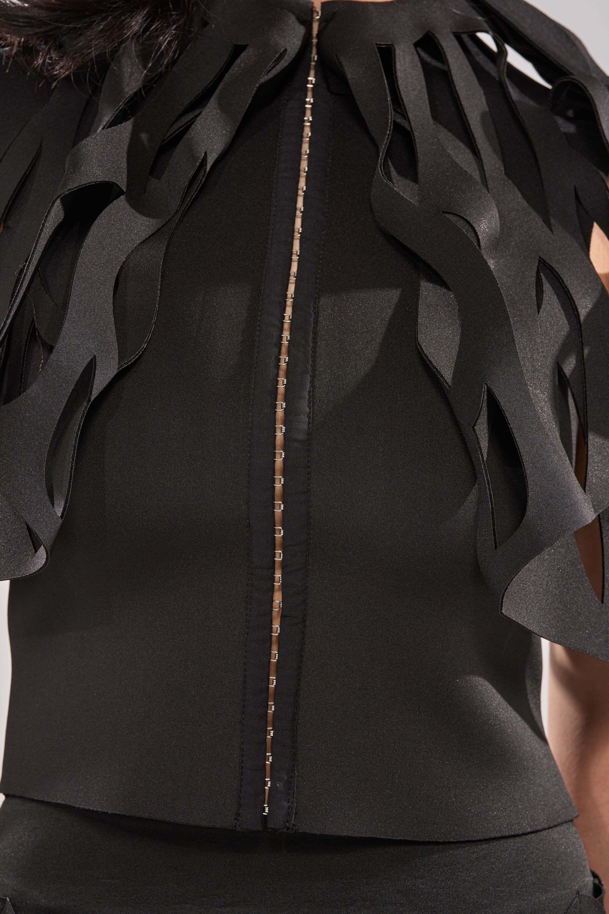A close-up of a person wearing the SEGA BLOUSE IN BLACK, an avant-garde top with sculptural cut-out detailing over the shoulders and chest, featuring a vertical beaded seam down the center. 6